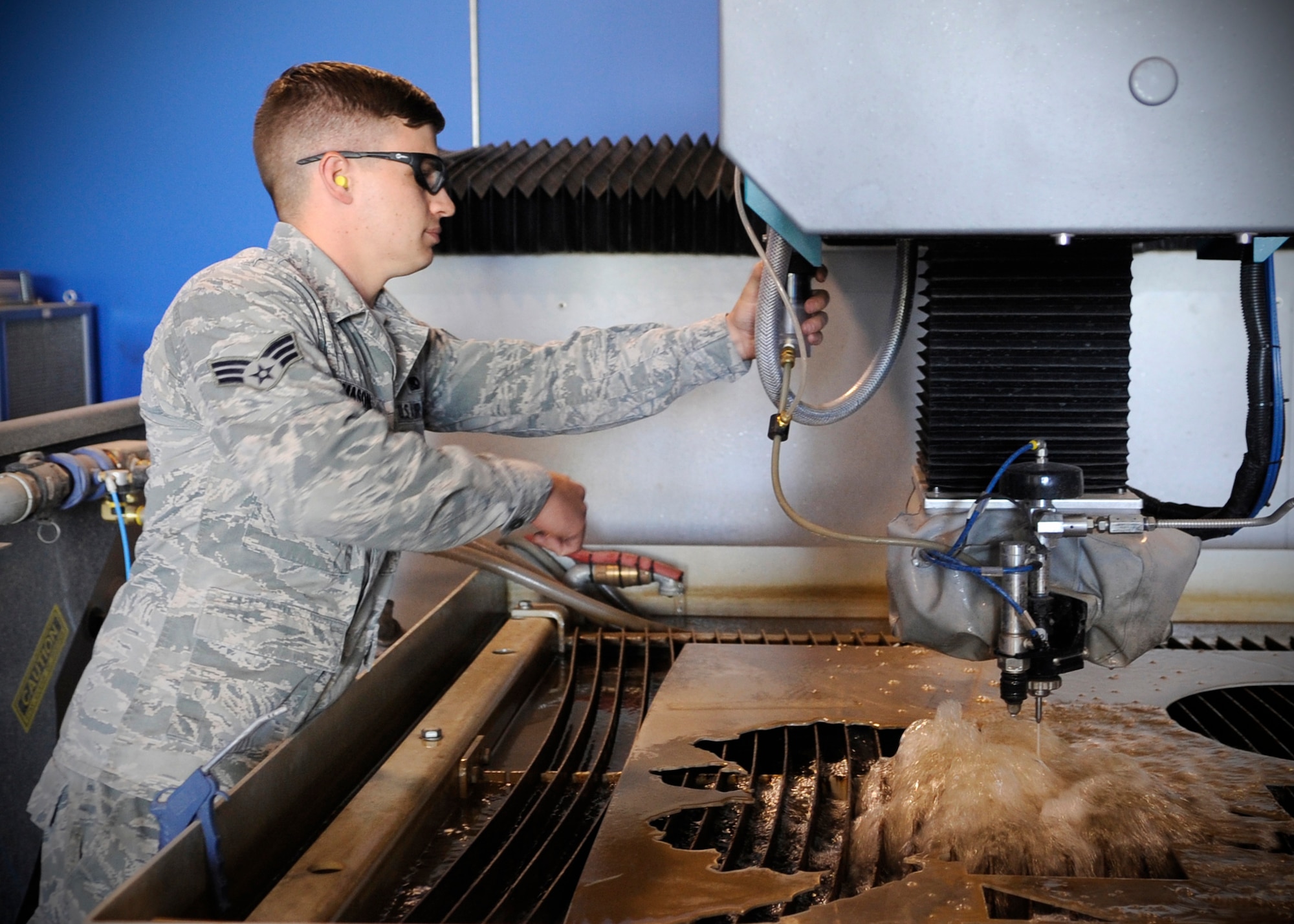 U.S. Air Force Senior Airman Robert Mason, 354th Maintenance Squadron metals technology journeyman, makes adjustments to a water jet while fabricating fuel caps for F-16 Fighting Falcons at Eielson Air Force Base, Alaska, July 22, 2013. Metals tech Airmen are certified to run the machine, which pierces metal with 55,000 pounds per square inch using water and an abrasive mixture. (U.S. Air Force Senior Airman Shawn Nickel/Released)