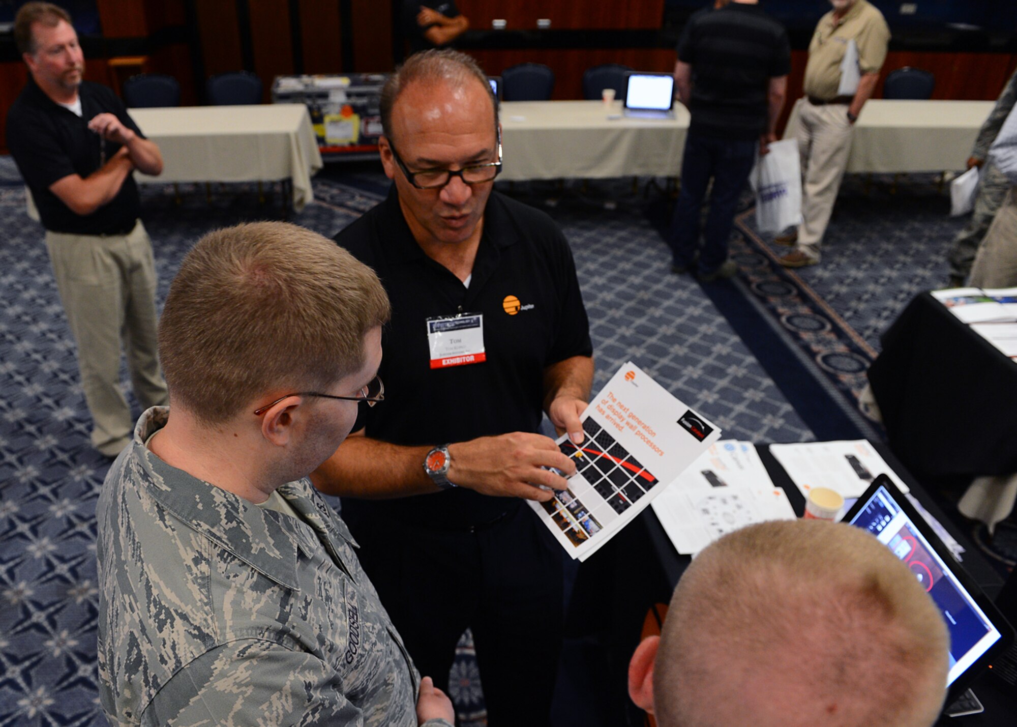 SPANGDAHLEM AIR BASE, Germany -- Tom Kopko, federal business development for Jupiter Systems, discusses his company's capabilities for network-based visual information collaboration with U.S. Air Force Staff Sgts. Josh Milller and Josh Goodsell, both from the 52nd Communications Squadron, at the 2013 Spangdahlem Technology Expo July 24, 2013. The Jupiter Systems demonstration included multiple-video displays intended for Defense Department operations centers. More than 25 exhibitors showcased their wares during the four-hour event. (U.S. Air Force photo by Staff Sgt. Daryl Knee/Released)