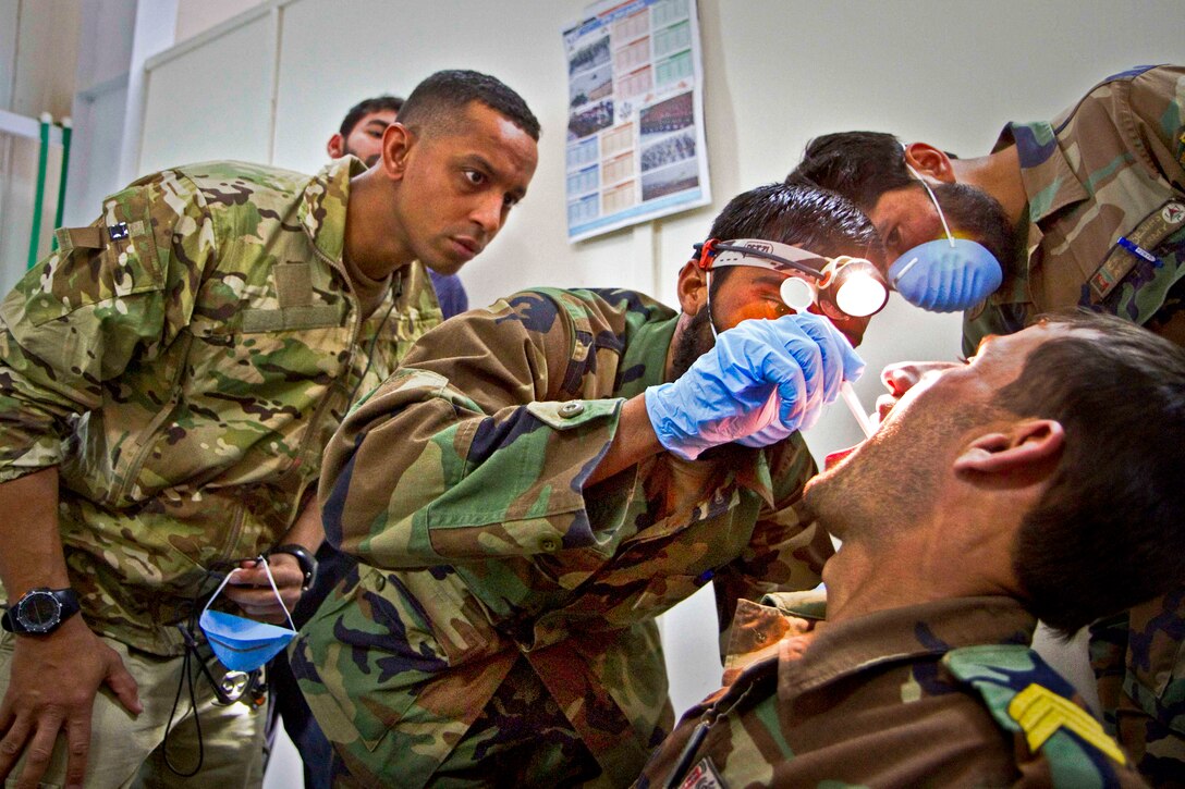 U.S. Army Capt. Abby Raymond, left, looks over the shoulder of an Afghan medic as he performs an oral exam on a commando during a basic dental class on Forward Operating Base Thunder in Paktya province, Afghanistan, July 21, 2013. Raymond, a dentist, is assigned to the 101st Airborne Division's 4th Brigade Combat Team.