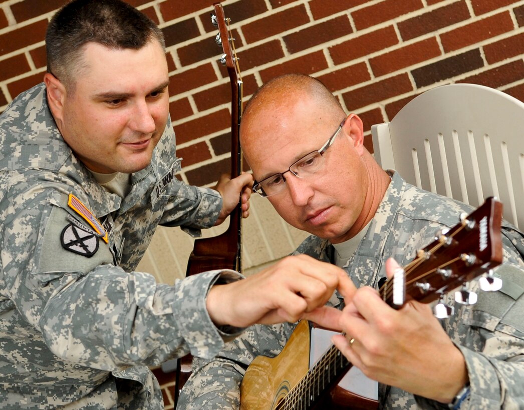 (From left) U.S. Army Sgt. Scott Black instructs Lt. Col. Eric. Whitelock, fellow Warrior Transition Unit healing soldier, where to place his fingers on the guitar during the “Music for Morale” program at Fort Eustis, Va., July 11, 2013. The program helps Soldiers improve memory while building camaraderie with fellow Soldiers. (U.S. Air Force photo by Staff Sgt. Wesley Farnsworth/Released)