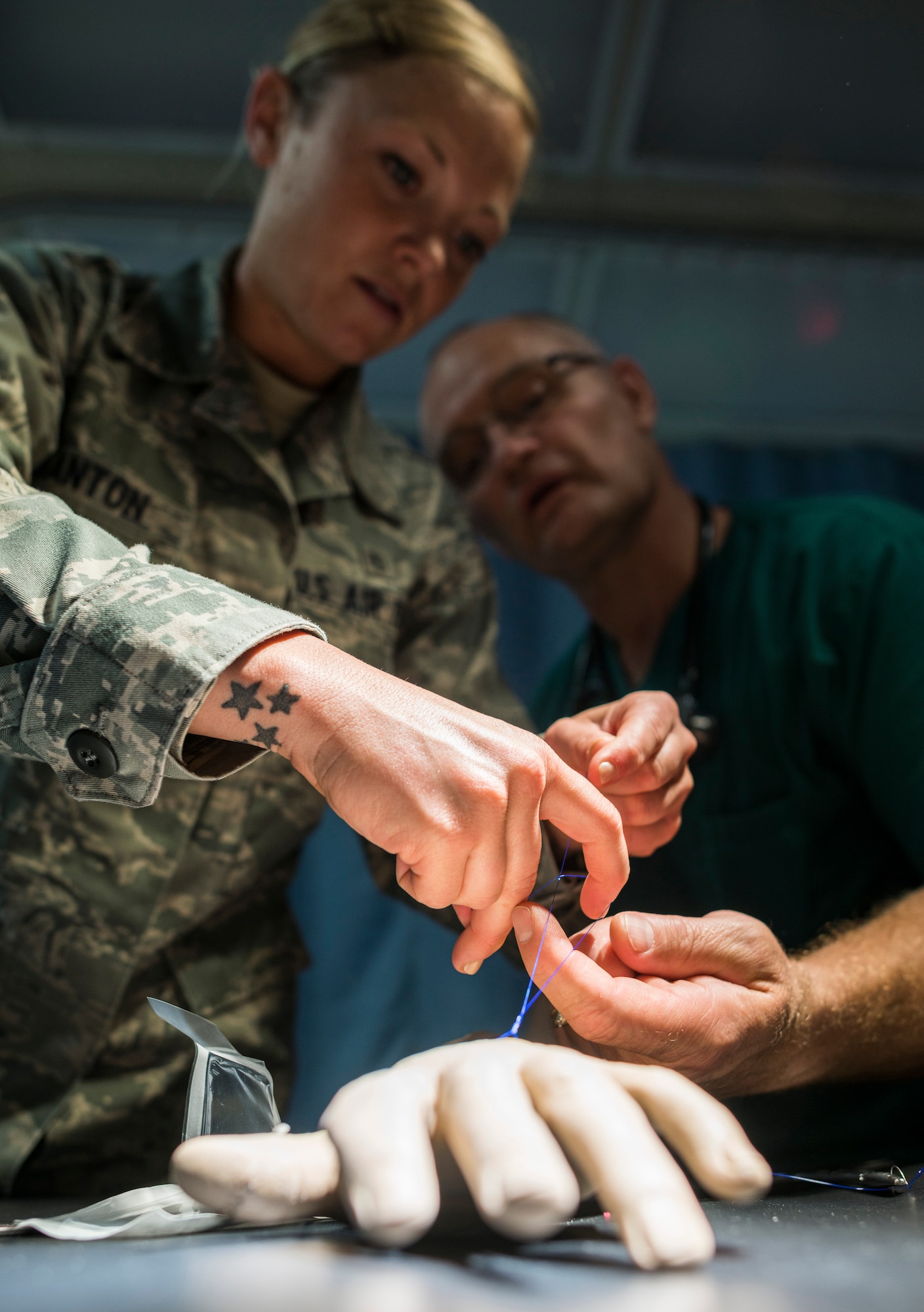 U.S. Air Force Lt. Col. (Dr.) Brandon Isaacs (right), an Air National Guardsman working as a 366th Medical Operations Squadron contract physician, teaches Senior Airman Megan Stanton (center), 366th MDOS medic, how to quickly tie a suture on a training dummy arm in the urgent care center at Mountain Home Air Force Base, Idaho, July 16, 2013. Isaacs taught Stanton single- and double-handed methods which will allow her to rapidly secure the sutures and increase her value in an operating room. (U.S. Air Force photo/Tech. Sgt. Samuel Morse)