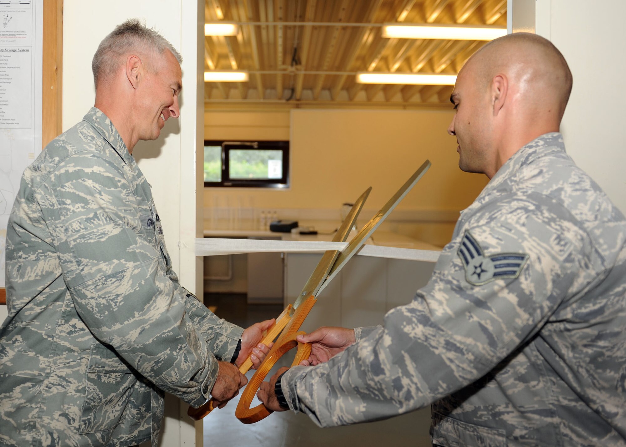 From left, Lt. Col. James Griffin, 100th Civil Engineer Squadron commander, and Senior Airman Joe Hamilton, 100th CES structural journeyman, cut the tape on a new sampling lab inside of the waste-water treatment plant July 25, 2013, in building 3 on RAF Mildenhall, England. The new water treatment plant is a Prime Base Engineer Emergency Force project for the 100th CES. A Prime BEEF project is done annually to ensure the 100th CES stays deployment ready. (U.S. Air Force photo by Airman 1st Class Preston Webb/Released)