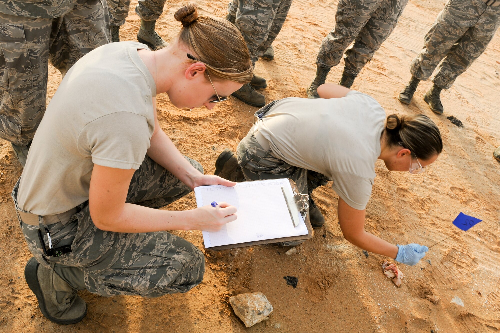 Airman 1st Class Caitlyn Iliff, 380th Expeditionary Force Support Squadron services apprentice, plots the location of a simulated portion of remains found as U.S Air Force Airman 1st Class Kristyn Grabendike, 380th EFSS apprentice marks the physical location during search and recovery training at an undisclosed location in Southwest Asia July 23, 2013. Iliff plots the location of each finding on a map; this technique is used when no GPS is available. Plotting the location of each item allows the team to come back to the exact location for retrieval.  Iliff hails from Spokane Wash., and is deployed from Fairchild Air Force Base, Wash. Grabenport is native to Riverside, Calif., and deployed from Shaw Air Force Base, S.C. (U.S Air Force photo by Staff Sgt. Joshua J. Garcia) 