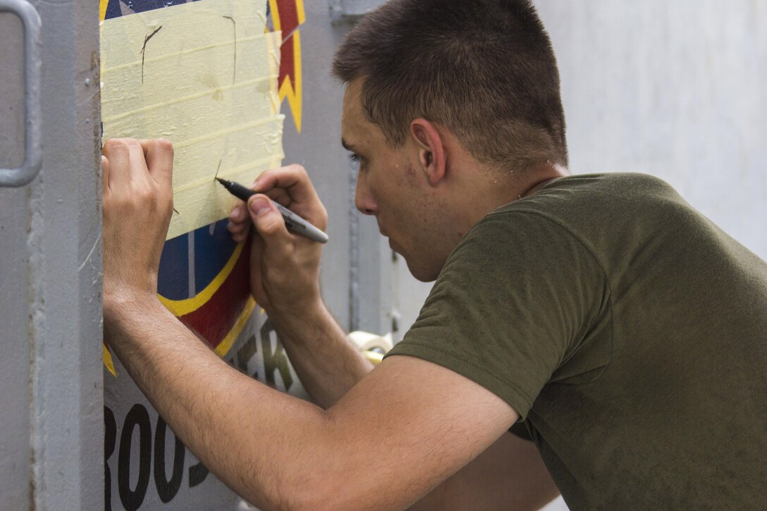 U.S. Marine Corps Cpl. Nicolas Belmer with Marine Medium Tiltrotor Squadron (VMM) 266 (Reinforced), 26th Marine Expeditionary Unit (MEU), traces the 26th MEU emblem incorporating a rooster on double-wide doors, on the flight deck of the USS Kearsarge (LHD 3), at sea, July 26, 2013. The 26th MEU is a Marine Air-Ground Task Force forward-deployed to the U.S. 5th Fleet area of responsibility aboard the Kearsarge Amphibious Ready Group serving as a sea-based, expeditionary crisis response force capable of conducting amphibious operations across the full range of military operations. (U.S. Marine Corps photo by Cpl. Kyle N. Runnels/Released)