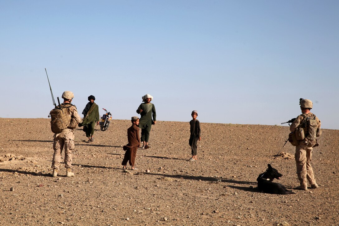 U.S. Marine Corps Cpls. William Ahern, left, and Adam Cook and his military dog, Falco, approach Afghan villagers during a patrol in Mohammad Abad village in Afghanistan’s Helmand province, July 23, 2013. Ahern, a radio operator, is assigned to Georgian Liaison Team 9, and Cook, a dog handler, and Falco are assigned to the 2nd Law Enforcement Battalion.