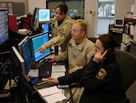 Air & Marine Operations Center director Tony Crowder (center) is assisted by Supervisor Detection Enforcement Officer Jessica Brand (left) and Detection Enforcement Officer Hidee Lehnert (right) at the Center's headquarters in California.