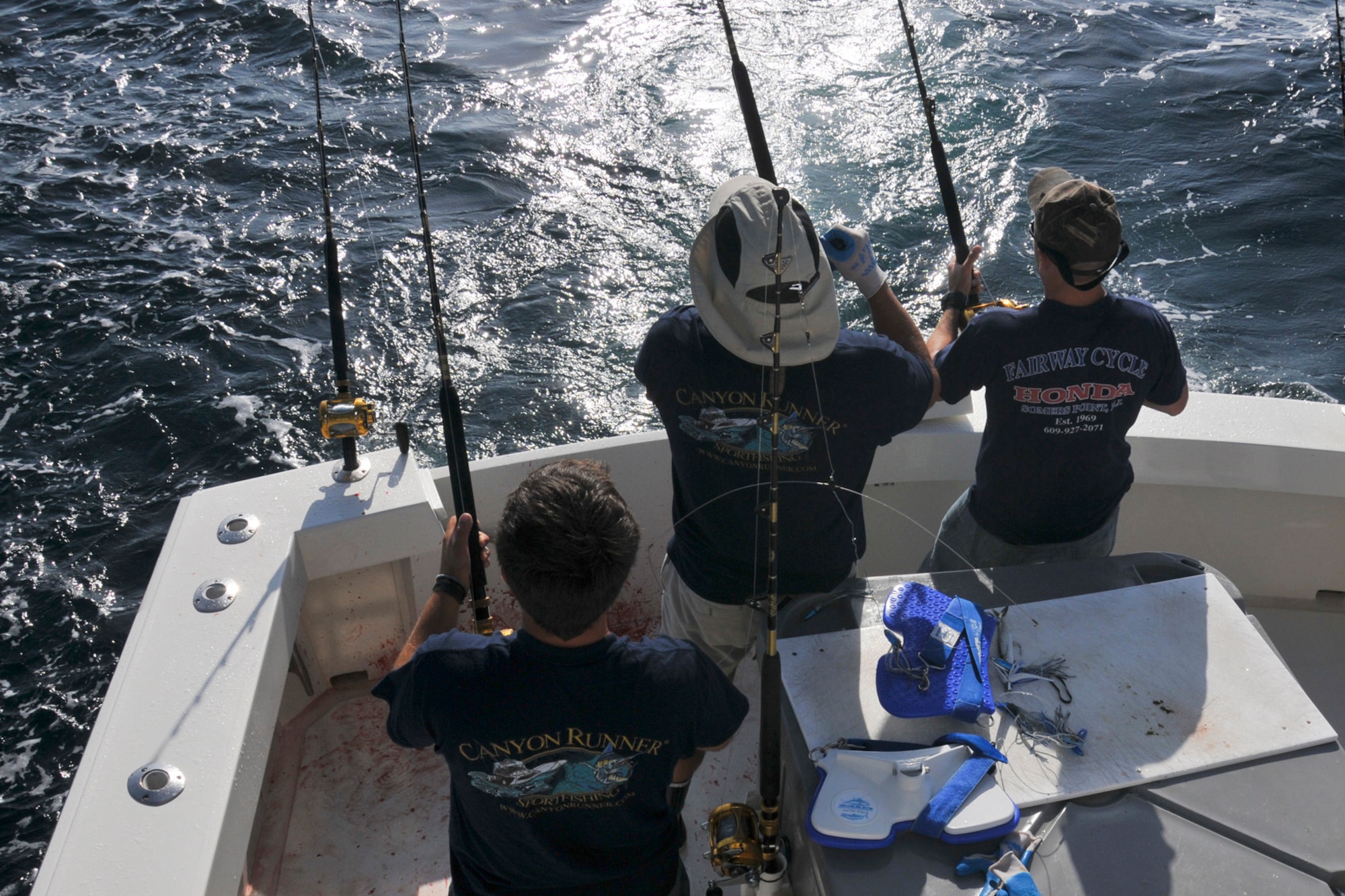 A picture of Captain Deane Lambros and Captain Greg Rybak, both of Canyon Runner Sportfishing, and U.S. Air Force Tech. Sgt. Keith Williams, weapons systems specialist with the 177th Fighter Wing, working together to reel in a mahi mahi.