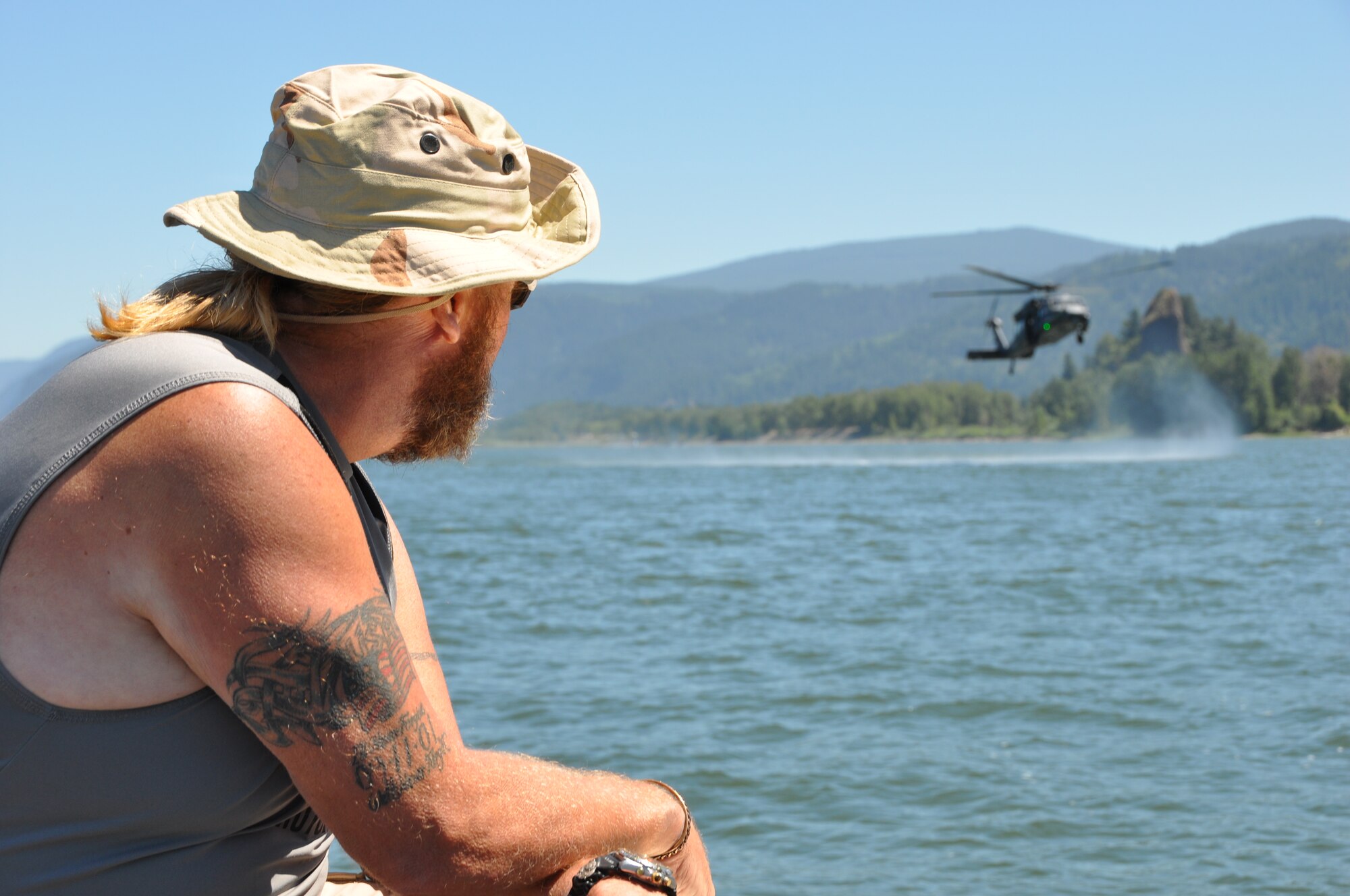 Mr. Jon Backa, dive master for the 304th Rescue Squadron, Portland International Airport, Ore. observes an HH-60G Pave Hawk helicopter from the 943rd Rescue Group, Davis-Monthan Air Force Base, Ariz., practice water rescue operations with pararescuemen from the 304th RQS in the Columbia River, near Rooster Rock State Park, Ore., July 27, 2013. (U.S. Air Force Photo/Staff Sgt. N. Daniel Delgado)