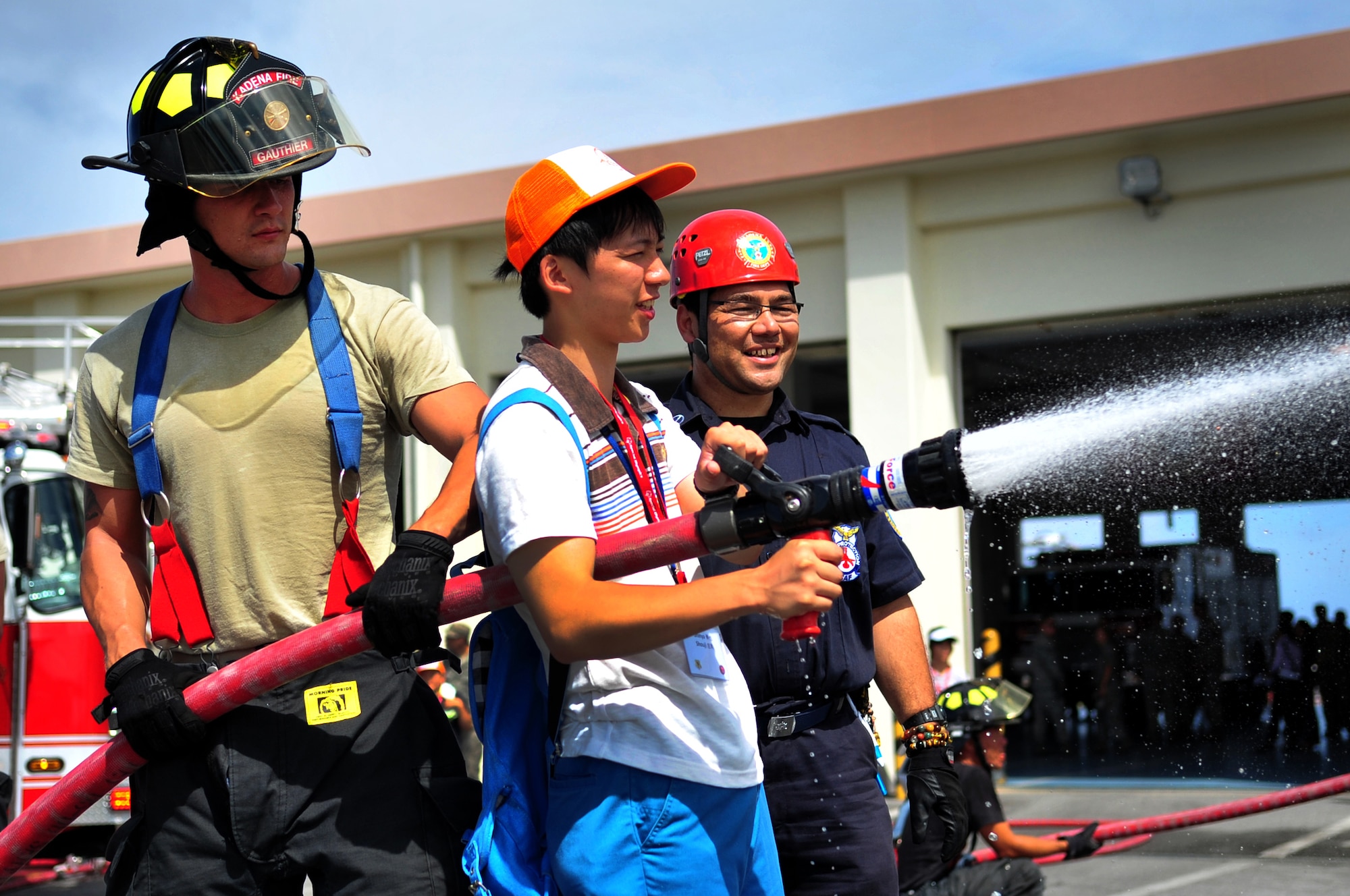 U.S. Air Force Airman 1st Class Robert Gauthier and Hiroshi Miyazato, 18th Civil Engineer Squadron firefighters, show a sixth-grader from Iitate Village how to use a fire hose during a school visit on Kadena Air Base, Japan, July 24, 2013. The students learned about the importance of rescue operations and how they pertain to natural disasters. (U.S. Air Force photo by Senior Airman E. N. Jacobs/Released)