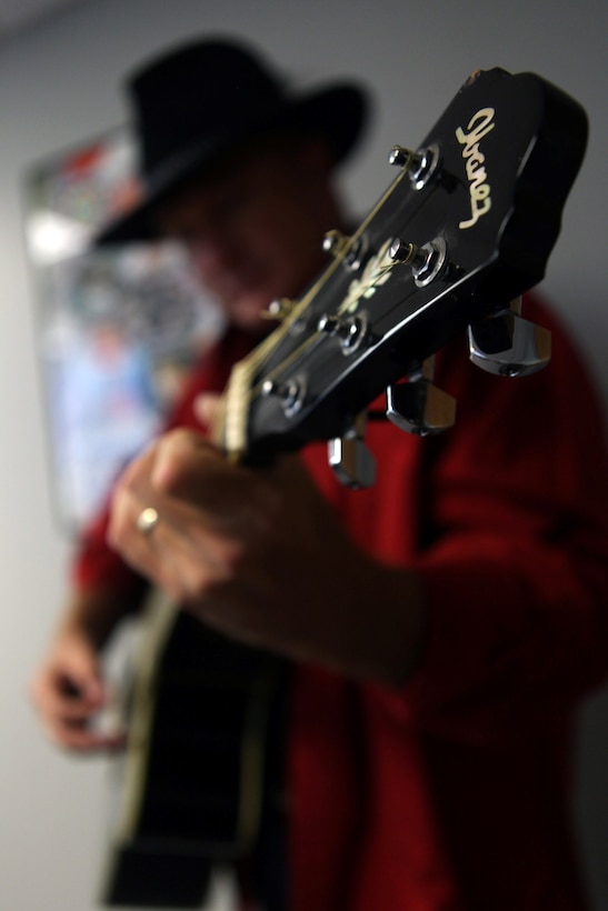 Lt. Col. Jerard A. Brewer, Marine Corps Installations-East Marine For Life officer in charge, plays his guitar next to a GI Jams poster featuring eight artists including himself aboard Marine Corps Base Camp Lejeune, July 26. Brewer said GI Jams is a network resource that supports service members who are muscially talented but do not have any contacts in the music industry.