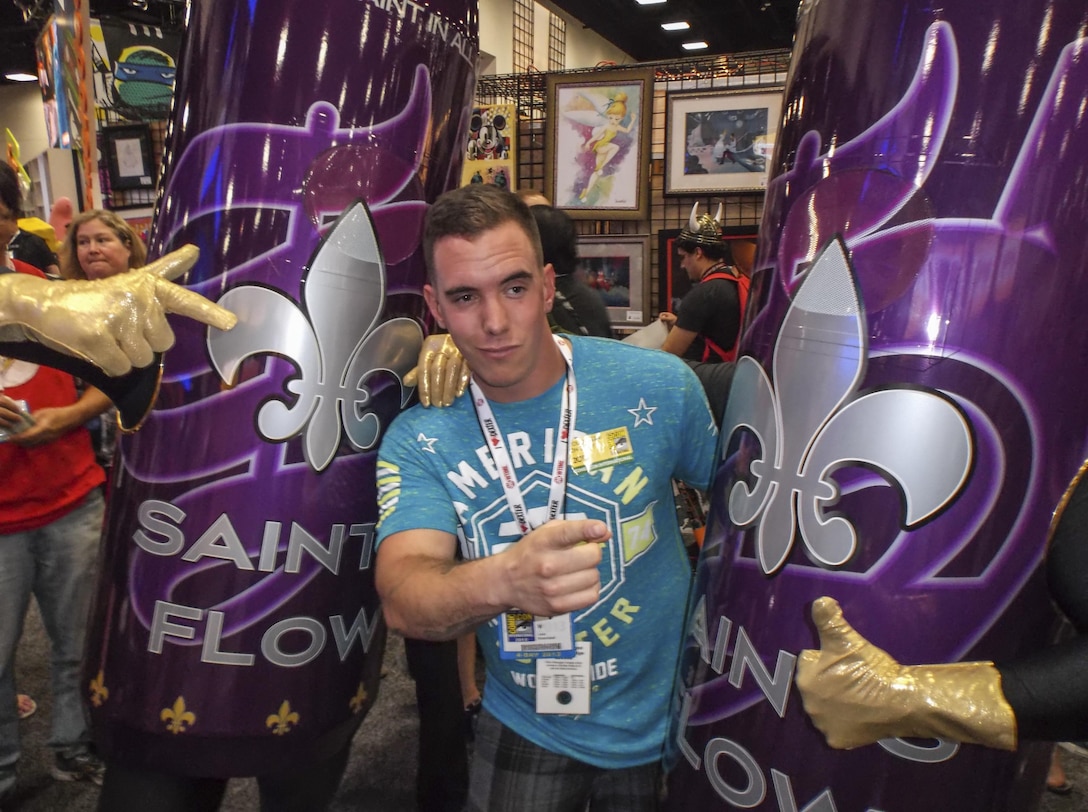Sgt. Leon Branchaud, the non-commissioned officer-in-charge of Combat Camera with Headquarters and Headquarters Squadron at Marine Corps Air Station Yuma, Ariz., poses with a pair of Saints Flow cans at the San Diego Comi-Con, July 18. Branchaud was attending Comi-Con as a part of a Single Marine Program volunteer opportunity.