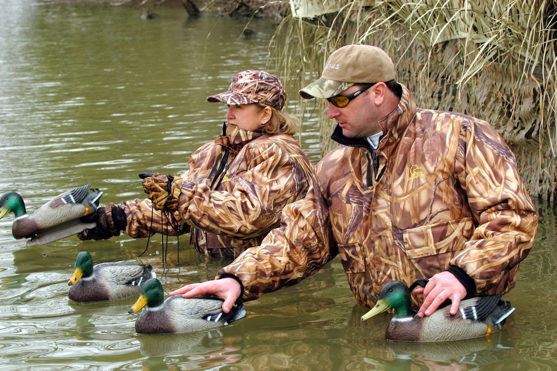 Hunters wearing hunting gear with personal flotation gear, place duck decoys.