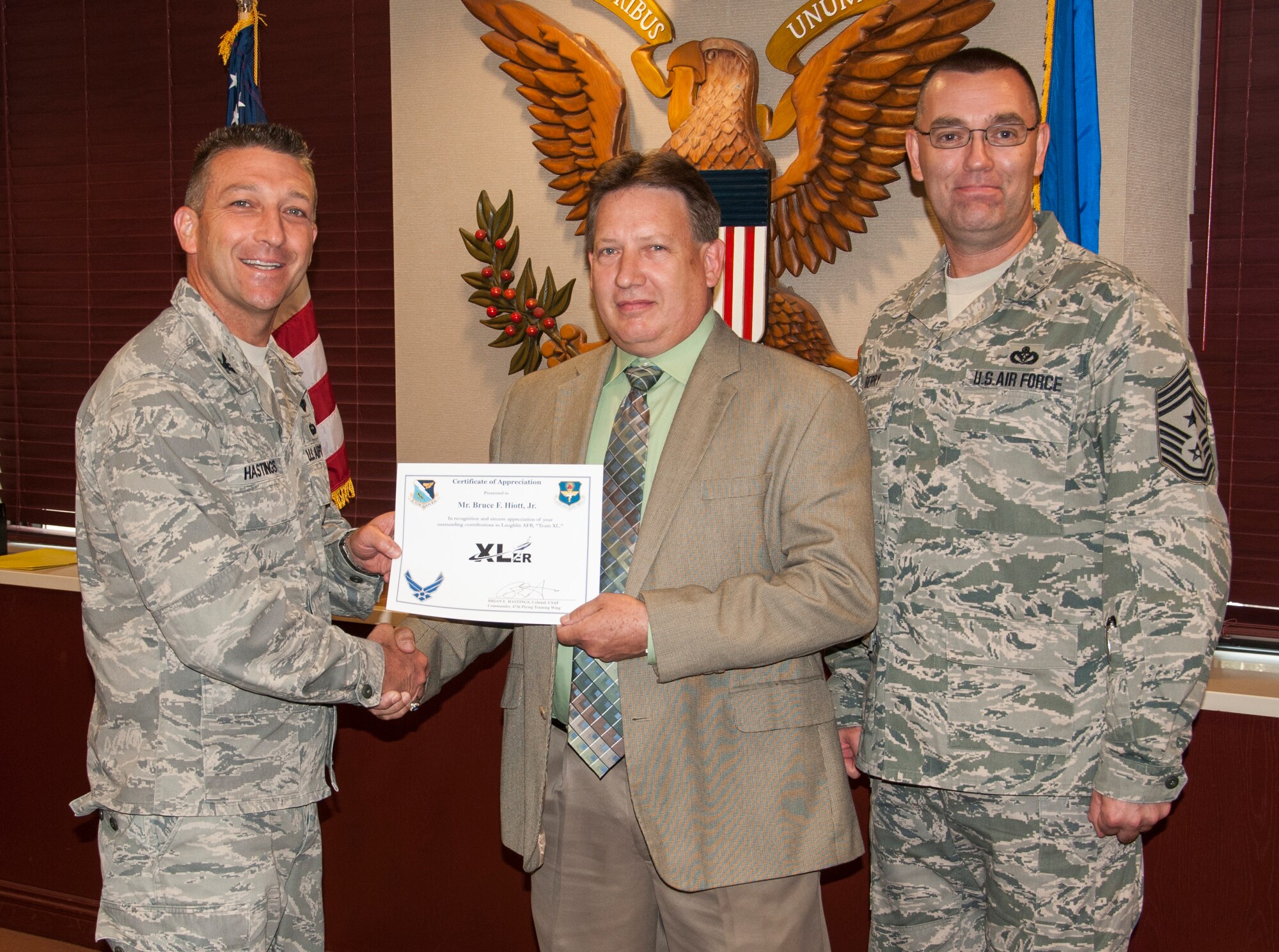 Bruce Hiott, Jr., 47th Force Support Squadron Laughlin club operations general manager, poses with Col. Brian Hastings, 47th Flying Training Wing commander, and Chief Master Sgt. Garry Berry, 47th FTW command chief, after being presented the XLer of the week award here July 16, 2013. The XLer is a weekly award chosen by wing leadership and given to those who consistently make outstanding contributions to Laughlin and their unit. (U.S. Air Force photo/Joel Langton)