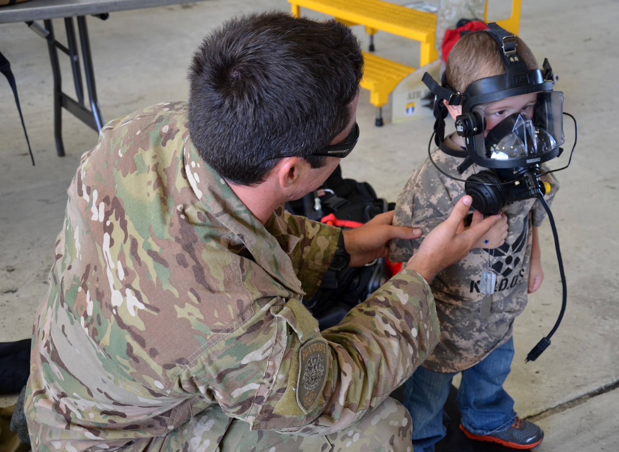 An Air Force Reserve pararescueman from the 308th Rescue Squadron helps an Air Force-dependent child try on a gas mask during the Kids Understanding Deployment Operations event at Patrick Air Force Base June 1, 2013. (U.S. Air Force photo/Tech. Sgt. Anna-Marie Wyant)