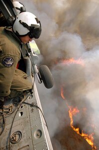 Aviation Warfare Systems Specialist 3rd Class Zach Sykora, attached to Helicopter Sea Combat Squadron Eight Five (HSC) 85, searches for a burning target to dump 420 gallons of water on.  HSC-85 has teamed up with the San Diego California Department of Forestry and Fire Protection to put out the wild fires blazing across Southern California.                                  