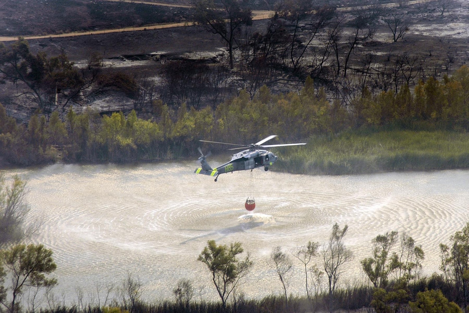 An MH-60S Seahawk helicopter retrieves water from a lake near the wildfires in San Diego. Helicopter Sea Combat Squadron (HSC) 85 has teamed up with the San Diego California Department of Forestry and Fire Protection to help put out the wildfires blazing across Southern California. 

U.S. Navy photo by Mass Communication Specialist Seaman Jon Husman 
