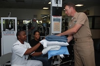 Hospital Corpsman Senior Chief (FMF/NAC) Trevor Dallas-Orr, Naval Medical Center San Diego Special Projects Officer for the Command Master Chief, hands blankets and pillows to Personnel Specialist 1st Class (SW/AW) William Clincy and his wife Iris during their stay at the temporary evacuation site. NMCSD provided community support and assistance during the San Diego wildfire which has claimed more than 240,000 acres of land in San Diego County. 