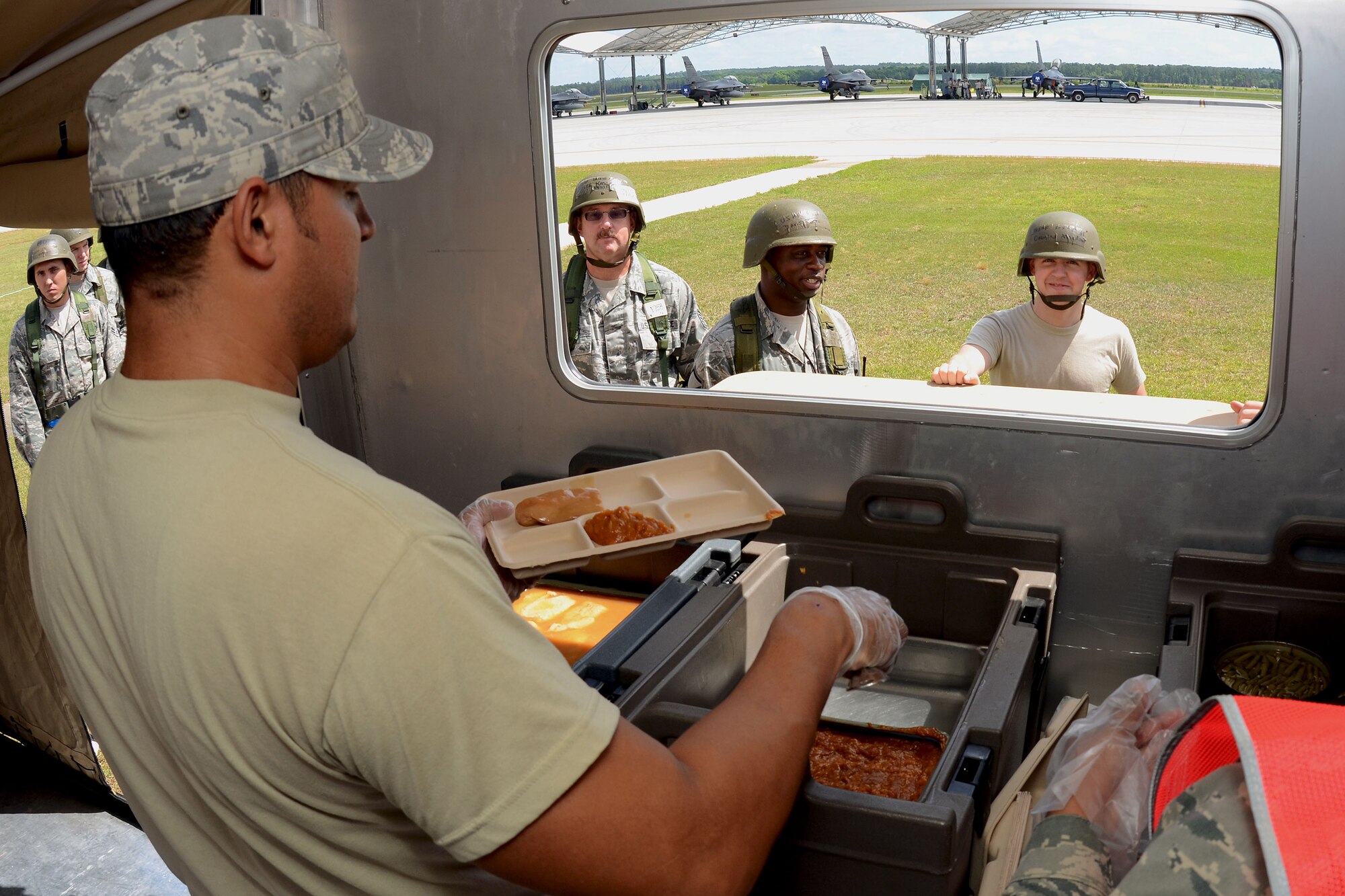 U.S. Air Force Airman 1st Class Luis Sanchez, a services specialist with the 169th Services Flight at McEntire Joint National Guard Base, South Carolina Air National Guard, serves food from the Single Palletized Expeditionary Kitchen during the June Unit Training Assembly Readiness Exercise, June 1, 2013. The SPEK is set up for flight line personnel, who can't afford the time to travel to the base dining facility, to have quick access to a hot meal. Members of the 169th Fighter Wing are preparing for a Certified Readiness Evaluation, which evaluates a unit's ability to process personnel and equipment from home station to a deployed location safely and efficiently, then operate and launch missions in a chemical combat environment.
(U.S. Air National Guard photo by Tech. Sgt. Caycee Watson/Released)