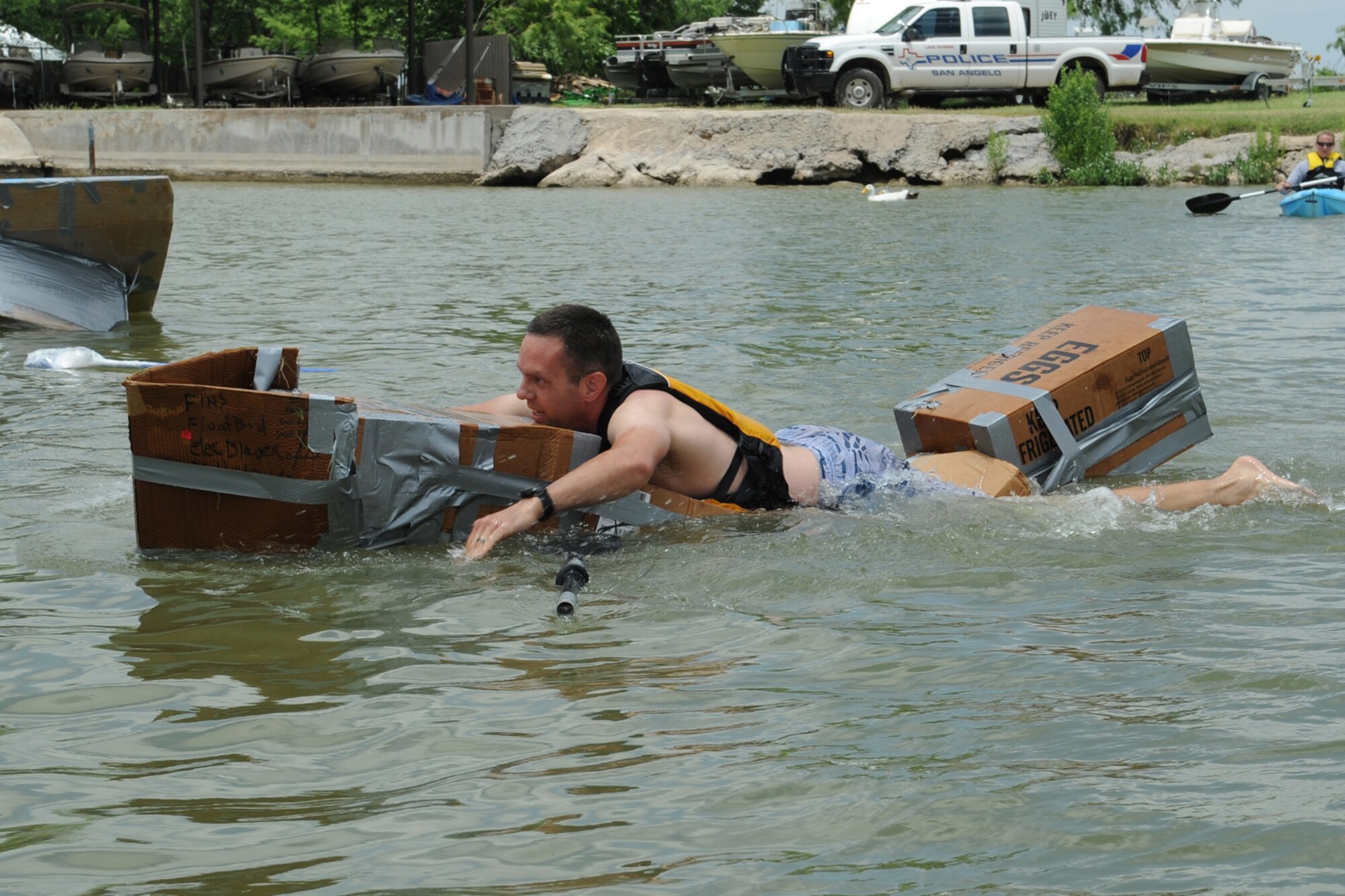 GOODFELLOW AIR FORCE BASE, Texas -- Lt. Col. Jeffrey McBride, 17th Mission Support Group Commander, paddles across Lake Nasworthy in his makeshift boat of cardboard, duct tape and milk jugs during the Build a Boat contest at the Goodfellow Recreation Camp, May 27. McBride won first place in the squadron category. (U.S. Air Force photo/ Staff Sgt. Laura R. McFarlane)