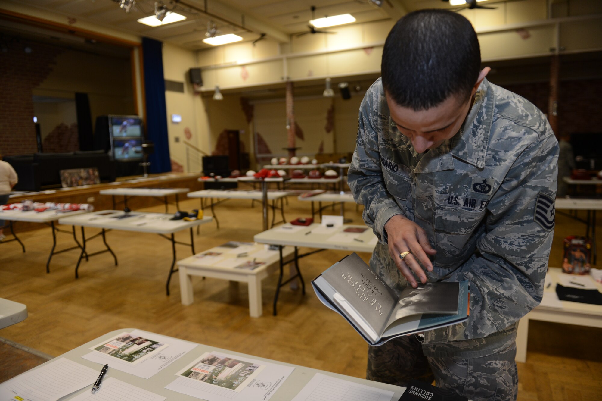 SPANGDAHLEM AIR BASE, Germany – U.S. Air Force Tech. Sgt. Fredric Rosario, 52nd Fighter Wing NCO in Charge of command post training from Berlington N.J., turns the pages of an autographed book during a silent auction inside the Brick House May 31, 2013.  The auction led to over $13,000 of donations for Operation Warm Heart throughout the day. (U.S. Air Force photo by Airman 1st Class Gustavo Castillo/Released)