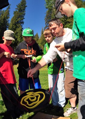 Special Agent John Cunniffe, camp counselor, and his group known as their camp name Wotanin, work together on the marble maze May 31, 2013, at YMCA Camp Reed during the team building session. The marble maze requires focus, teamwork and strategy to make the marble go through the maze without dropping in the holes. (U.S. Air Force photo by Senior Airman Earlandez Young/Released)   