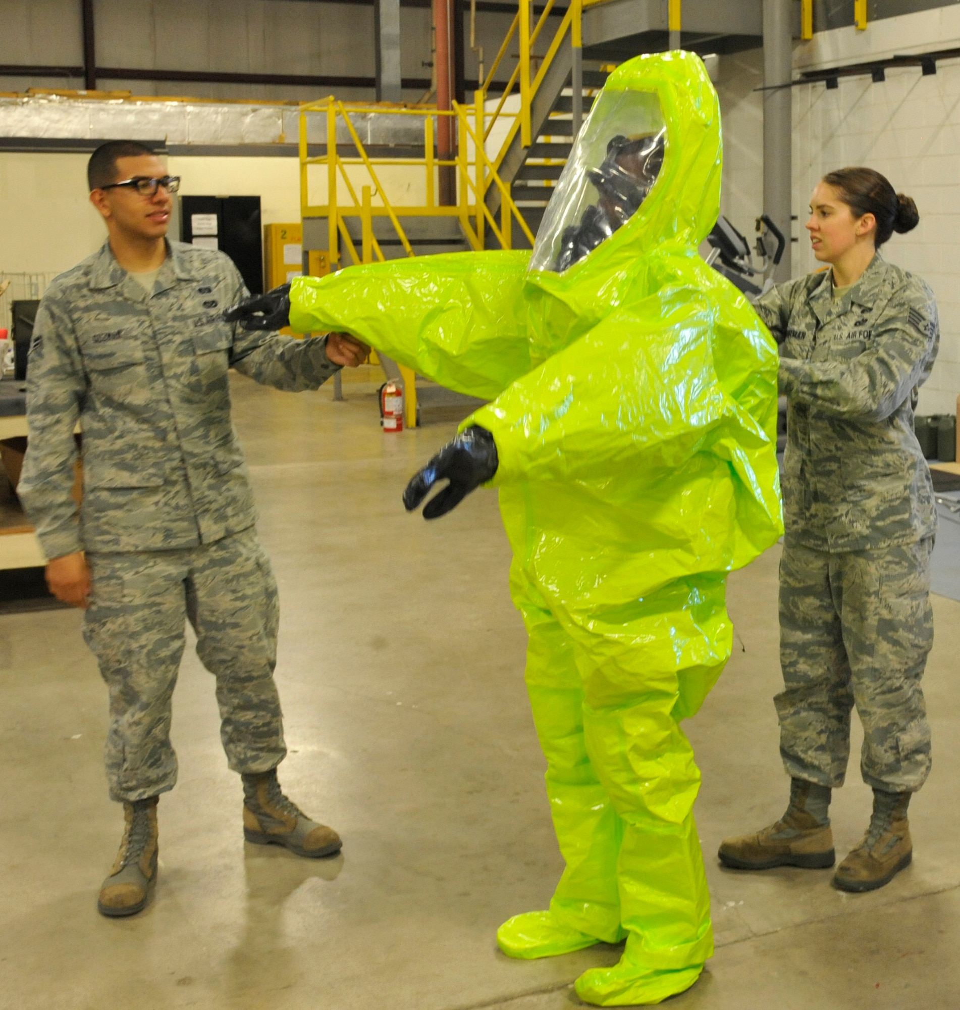 Staff Sgt. Rebecca Buhrman, 509th Civil Engineer Squadron NCO in charge of emergency management logistics, and Airman 1st Class Alfredo Guzman, 509th CES journeyman, assist Airman 1st Class Brandon Stone, 509th CES apprentice, with putting on a Level-A suit at Whiteman Air Force Base, Mo., May 22, 2013. Airmen wear this fully-encapsulated, chemical-resistant suit to enter hazardous or contaminated environments, as it is designed to prevent any air from entering or exiting. (U.S. Air Force photo by Airman 1st Class Keenan Berry/Released)