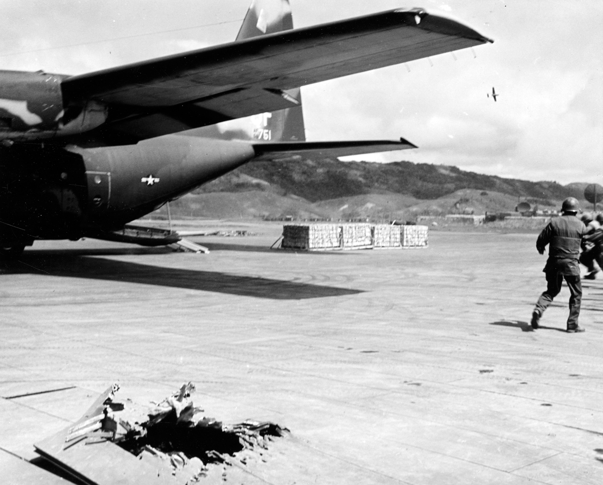 Marines rush to unload cargo from a USAF C-130 at Khe Sanh while a forward air controller (FAC) flies cover in the O-2 in the background. The FAC could quickly call in close air support to keep the enemy from firing mortar rounds at the C-130. Note the hole left in the ramp by a mortar. (U.S. Air Force photo)