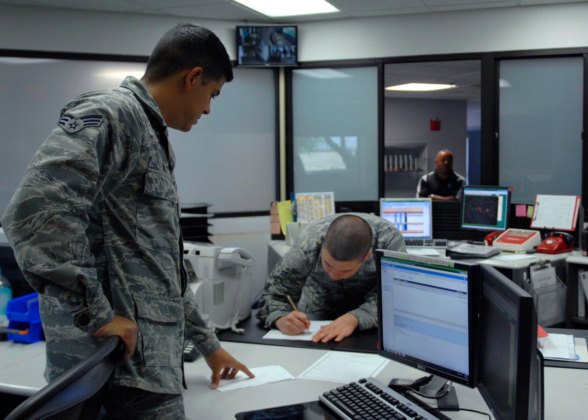 U.S. Air Force Senior Airman Ralph Ruiz and Airman 1st Class Chris Greg, both from the 355th Operations Support Squadron base operations, complete paperwork after coordinating with other agencies, such as 355th Fighter Wing Command Post, on runway activities at Davis-Monthan Air Force Base, Ariz., June 4, 2013. One of the primary duties of Airmen assigned to base ops is to track inbound and outbound aircraft. (U.S. Air Force photo by Airman 1st Class Saphfire Cook/Released)