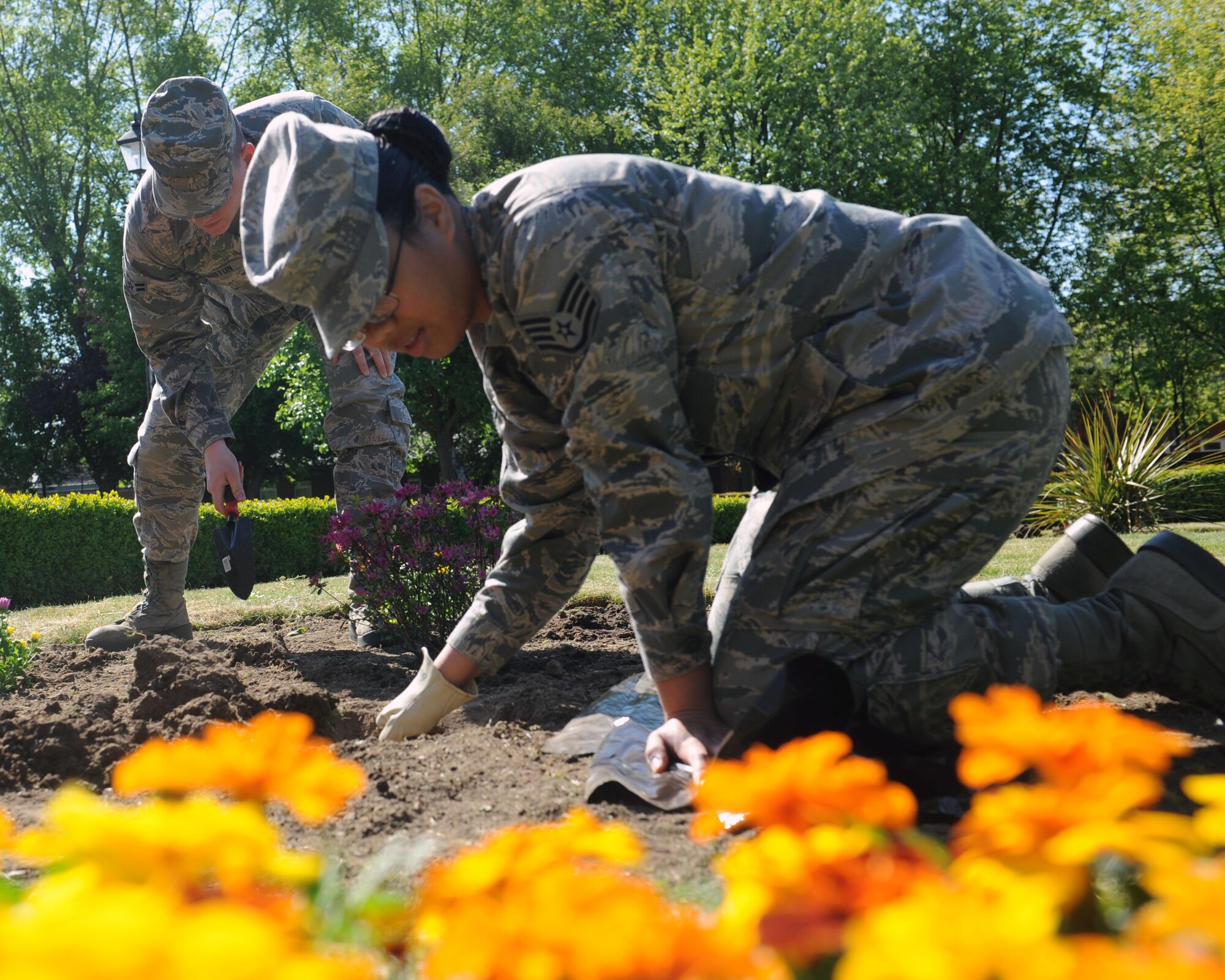 Front, Staff Sgt. Jerilyn Quintanilla, 100th Air Refueling Wing public affairs photojournalist, plants flowers as part of a base clean-up June 7, 2013, at RAF Mildenhall, England. Quintanilla planted flowers to improve the overall appearance of the base. (U.S. Air Force photo by Airman 1st Class Preston Webb/Released)