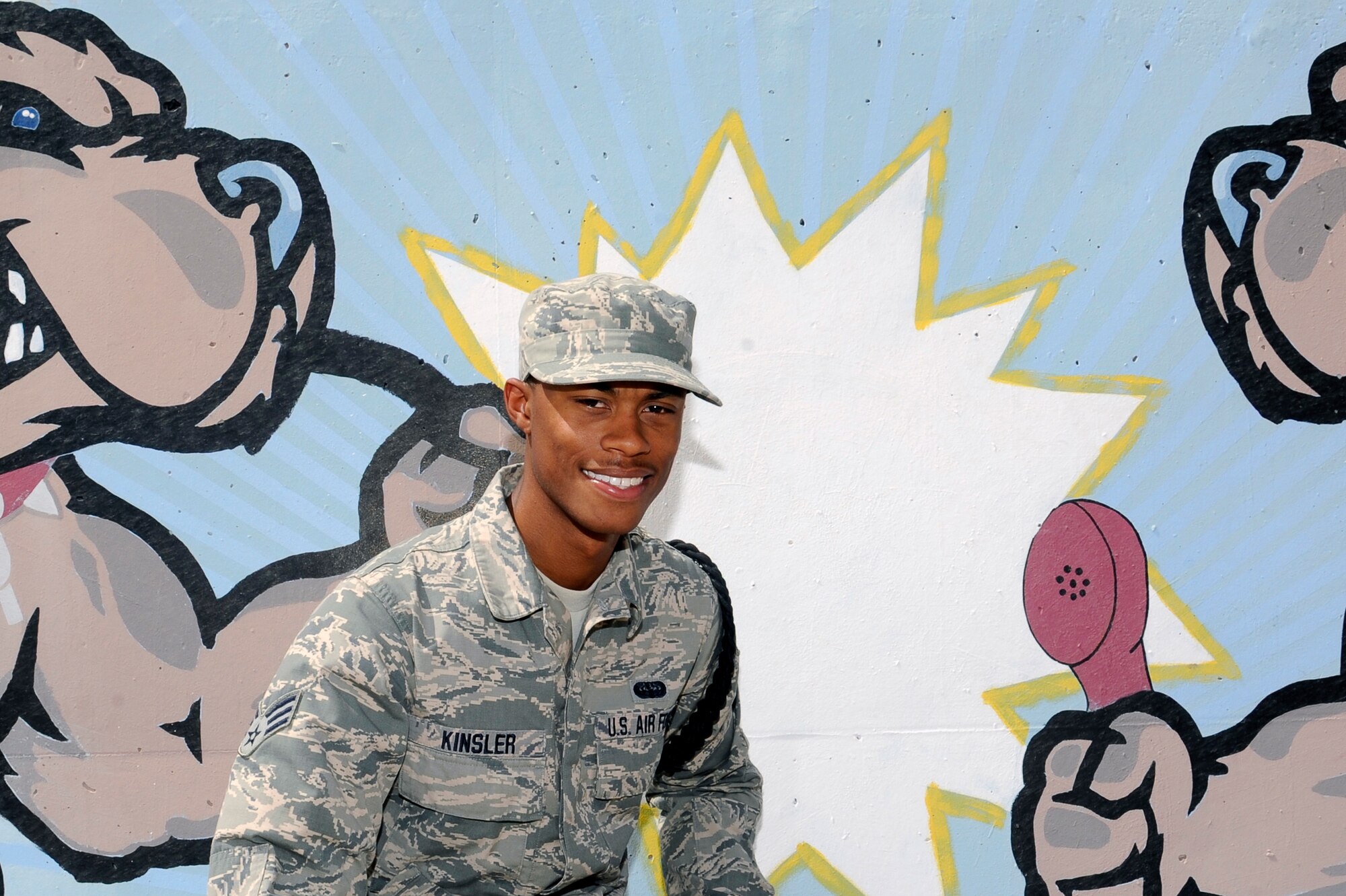 Senior Airman Corey Kinsler, 386th Expeditionary Communications Squadron, poses in front of artwork that depicts the squadron mascot with various representations of communication at the 386th Air Expeditionary Wing, Southwest Asia, June 7, 2013. Kinsler was awarded this weeks "Rock Solid Warrior" designation by the 386th Top 3 Council.  Kinsler’s job as a system administrator is to provide high level support for the various communication applications and systems on base.  (U.S. Air Force photo by Staff Sgt. Austin Knox)