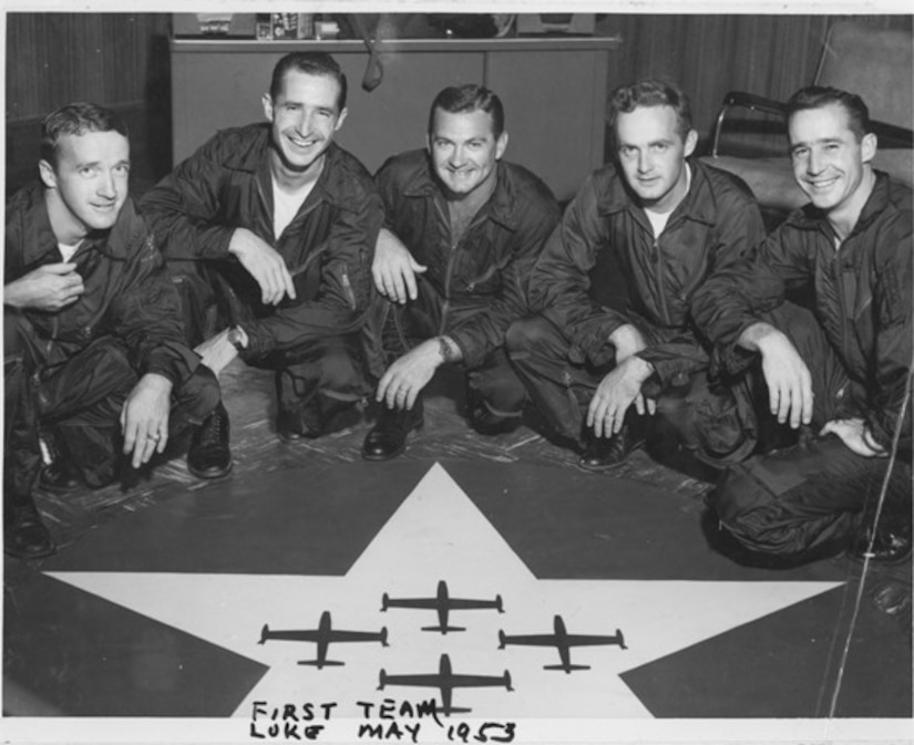 Five smiling pilots kneel in a row.