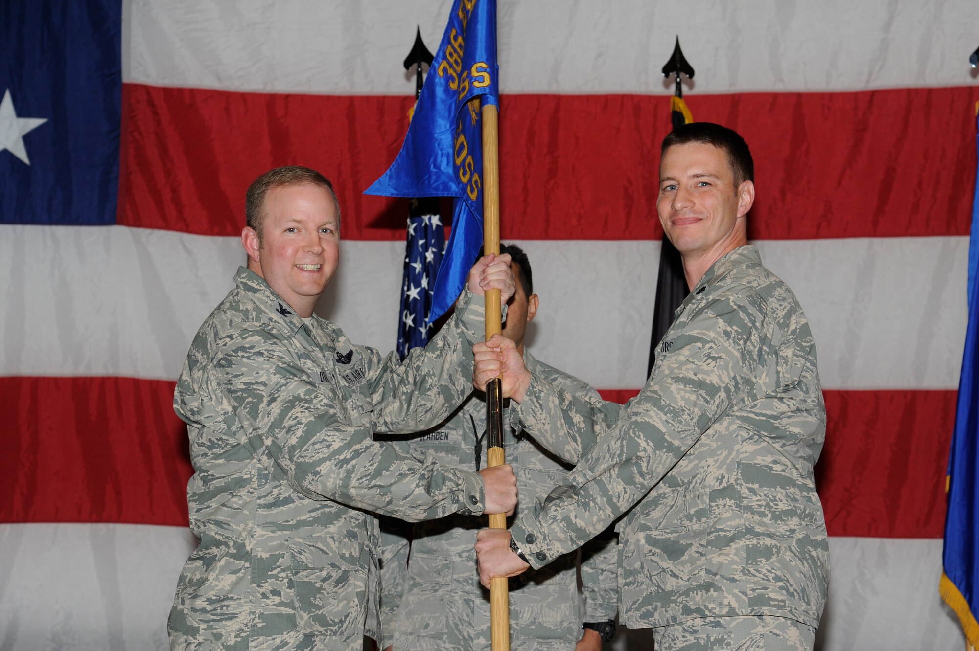 Colonel Jeffrey DeVore, 386th Expeditionary Operations Group commander, left, passes the 386th Expeditionary Operations Support Squadron guidon to Lt. Col. John Schutte during a change of command ceremony at an undisclosed location in Southwest Asia June 6, 2013. Schutte assumed command of the 386th EOSS from Lt. Col. Eric Hook. (U.S. Air Force photo by Staff Sgt. Austin Knox)