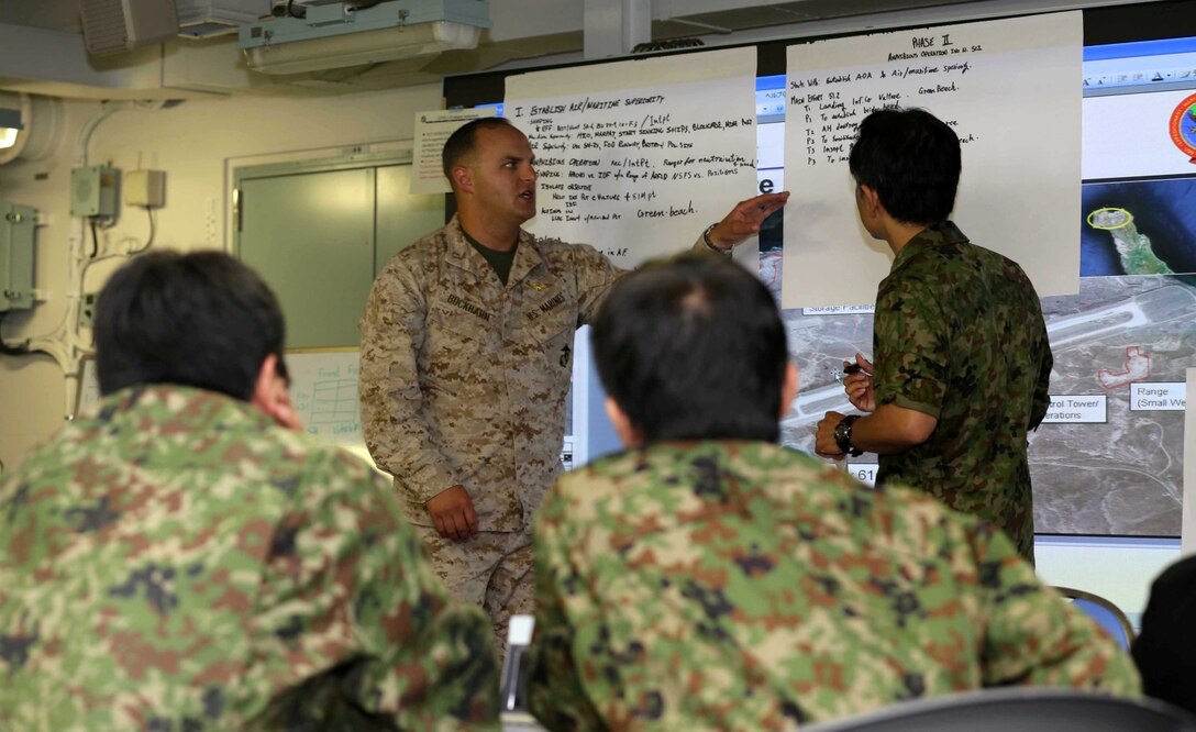 Capt. Philipp Buckhahn, 11th Marine Expeditionary Unit assistant air officer, assist with instructing members of the Japanese Self Defense Force about amphibious operations during a planning exercise on board the Japanese ship Hyuga at Naval Base San Diego June 6.  The planning exericse gave Marines and sailors a chance share how U.S. ground components and maritime components work together to conduct amphibious operations.  This training is part of Exercise Dawn Blitz, which is scenario-driven exercise that refocuses Navy and Marine Corps and coalition forces in their ability to conduct complex ambibious operations.