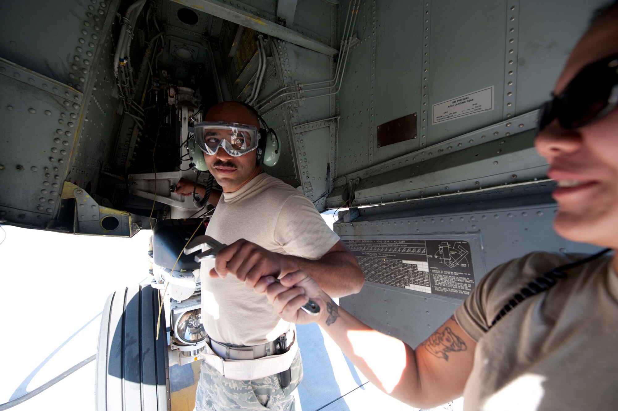 U.S. Air Force Staff Sgt. Kayla Reeh, 376th Expeditionary Aircraft Maintenance Squadron instrument and flight contol specialist, hands a wrench to Master Sgt. Chris Wieticha, 376th EAMXS hydraulic technician, so he can let air out of the nose strut in the KC-135's front landing gear on the flightline at Transit Center at Manas, Kyrgyzstan, June 7, 2013. Proper maintenance of the wheel hydraulics ensures safe take-off and landing. (U.S. Air Force photo/Staff Sgt. Robert Barnett)