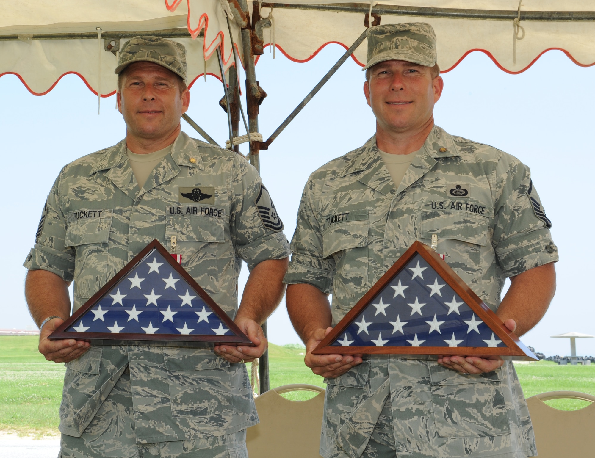 U.S. Air Force Master Sgt. Jared Tuckett, 390th Intelligence Squadron formal training section chief (left), and twin brother Master Sgt. Jason Tuckett, 3d Intelligence Squadron mission management superintendent (right), receive U.S. flags during their retirement ceremony on Torii Station, Japan, June 10, 2013. The brothers retired after 41 years of combined service in the U.S. Air Force as cryptologic linguist analysts. (U.S. Air Force photo by Airman 1st Class Keith A. James/Released)