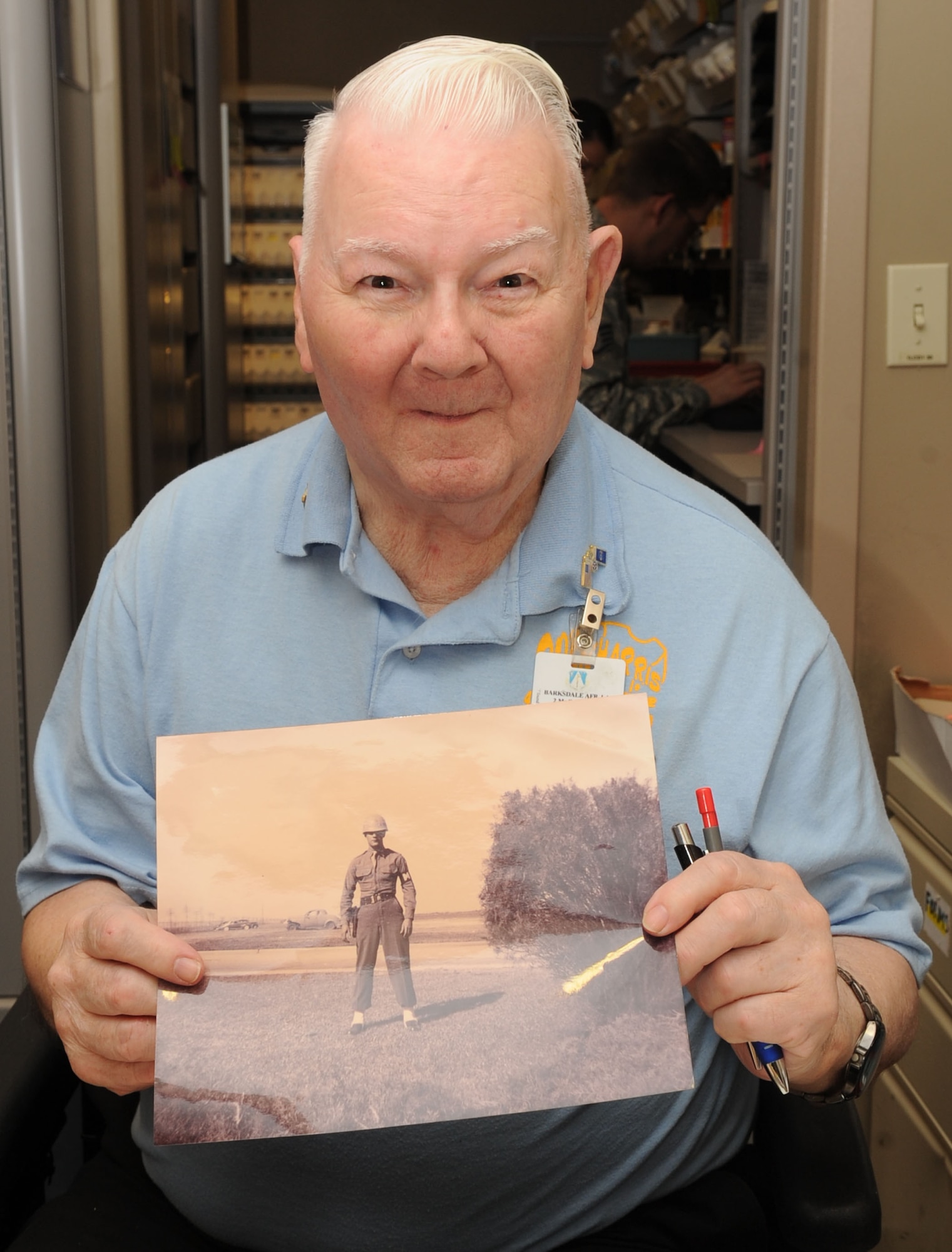 Dock Harris, 2nd Medical Group pharmacy volunteer, poses with a photo of himself in the Army Air Corps in 1949 on Barksdale Air Force Base, La., June 11, 2013. Harris served 13 years in the military before he was injured in Korea in 1951. He has volunteered for the pharmacy for the past 32 years. (U.S. Air Force photo/Senior Airman Kristin High)