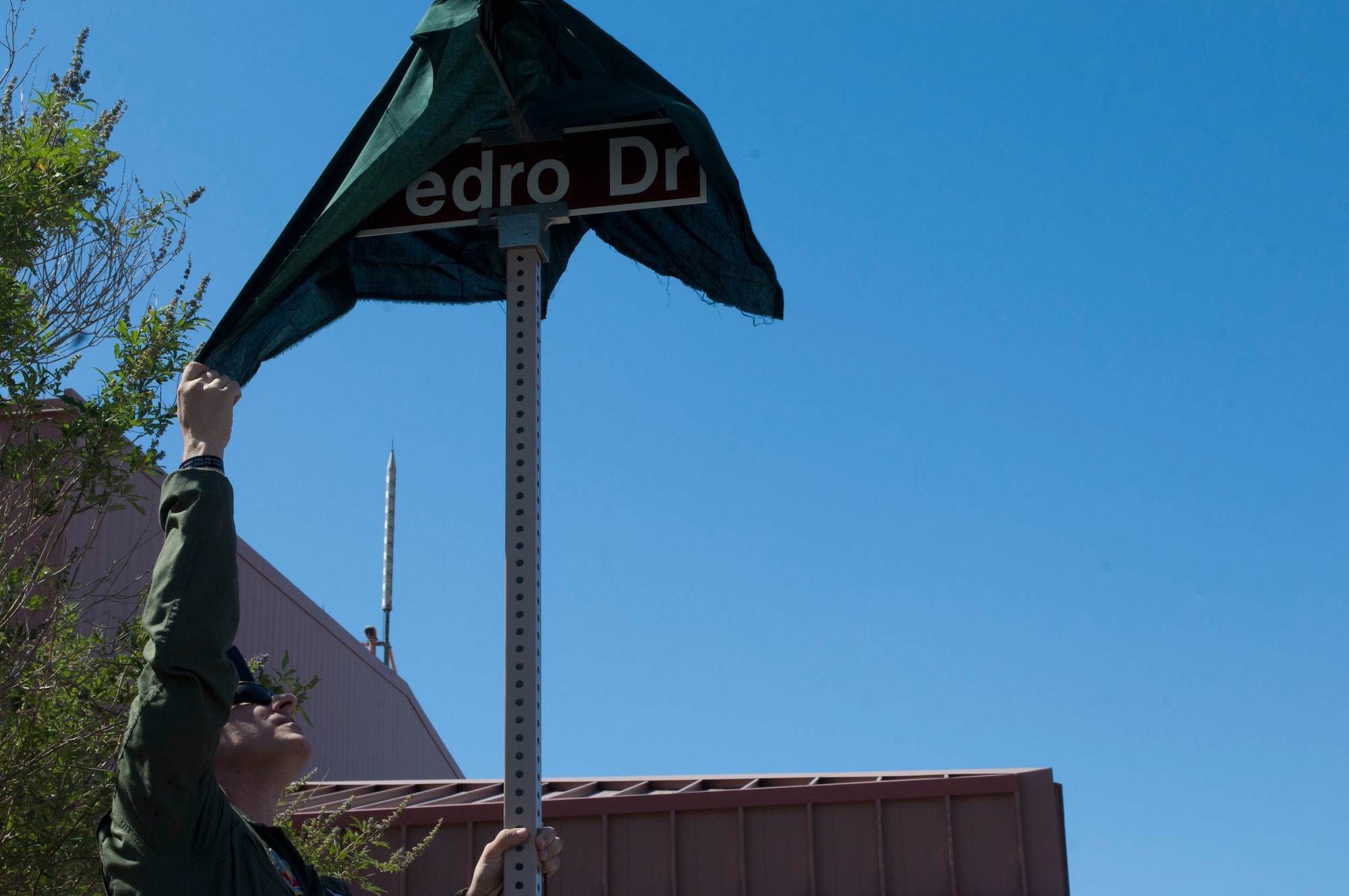 Staff Sgt. Christopher Cholet, 66th Rescue Squadron flight engineer instructor, pulls the cover off a new street sign during a street naming ceremony June 10, 2013, at Nellis Air Force Base, Nev. Pedro Drive is named in honor of the crew of the HH60G Pave Hawk helicopter, call sign "PEDRO 66" that was shot down and crashed three years ago in Helmand Province, Afghanistan. (U.S. Air Force photo by Airman 1st Class Joshua Kleinholz)
