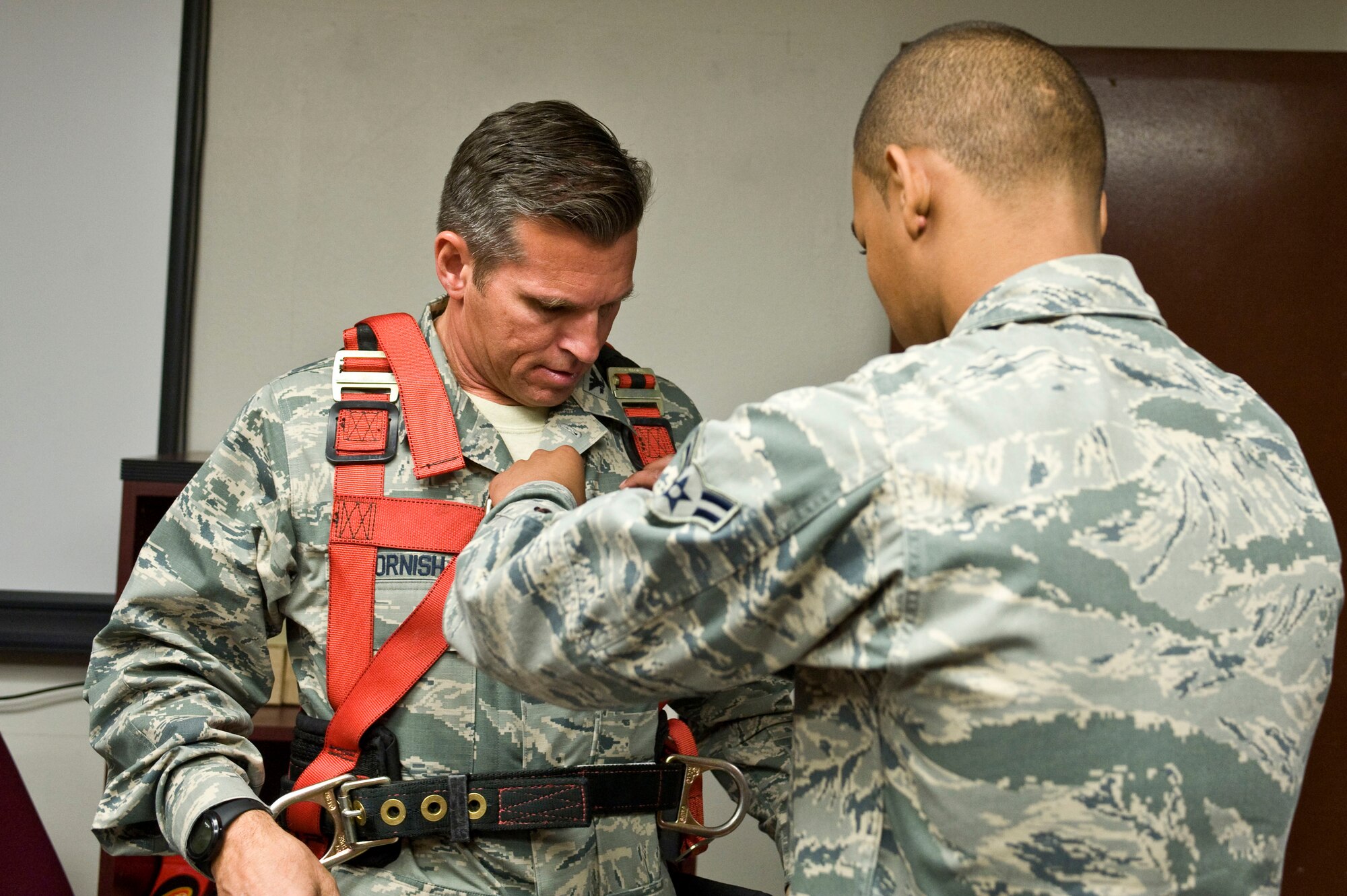 Airman 1st Class Bruce Jackson, 99th Communications Squadron airfield systems apprentice, assists Col. Barry Cornish, 99th Air Base Wing commander, with a climbing harness before the radio tower climbing demonstration June 7, 2013, at Nellis Air Force Base, Nev. Making sure the harness fits properly is important to avoid injury. (U.S. Air Force photo by Senior Airman Matthew Lancaster)