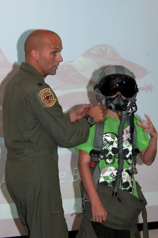 Lt. Col. Kevin Gordon, 64th Aggressor Squadron director of operations, explains the functions of life support equipment modeled by Austin Fitzgerald, a  survivor of childhood cancer, at the 64th AGRS briefing room June 8, 2013, at Nellis Air Force Base, Nev. The visit was hosted by the pilots of the 64th AGRS with help from the 65th AGRS, the 547th Intelligence Squadron, the United States Air Force Air Demonstration Squadron Thunderbirds and the 99th Civil engineer squadron for the Candlelighters Childhood Cancer Foundation of Nevada. (U.S. Air Force Photo by Staff Sgt. Gregory Brook)