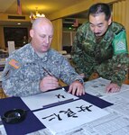 CAMP ASAKA, JAPAN - Army Sgt. 1st Class Tony Bowling (left), first sergeant for Headquarters Company, 8th Theater Sustainment Command out of Fort Shafter, Hawaii, gets a lesson in the art of Calligraphy from Sgt. Maj. Kazuhiko Shimizu of the JGSDF's 104th General Support Battalion, Dec. 3, 2008, at the camp's Freedom Room. Bowling, who hails from Canton, Ill., is one of more than 1,000 American Soldiers, Sailors, Marines and Airmen participating in Yama Sakura 55, along with their counterparts from the Japanese ground, air and maritime services. Yama Sakura is a bilateral U.S.-Japan, computerized command post exercise designed to better the defense of Japan, and to protect each country's interests throughout East Asia.