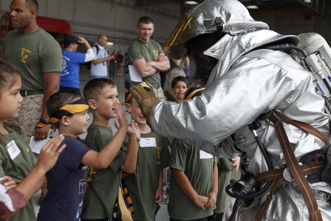 A Marine with Aircraft Rescue and Firefighting gives children high fives before showing a demonstration during a Junior Jarhead Day hosted by Marine Aircraft Group 16 aboard Marine Corps Air Station Miramar, Calif., June 8. ARFF Marines let children sit in the P-19 fire truck and learn about the gear they use.