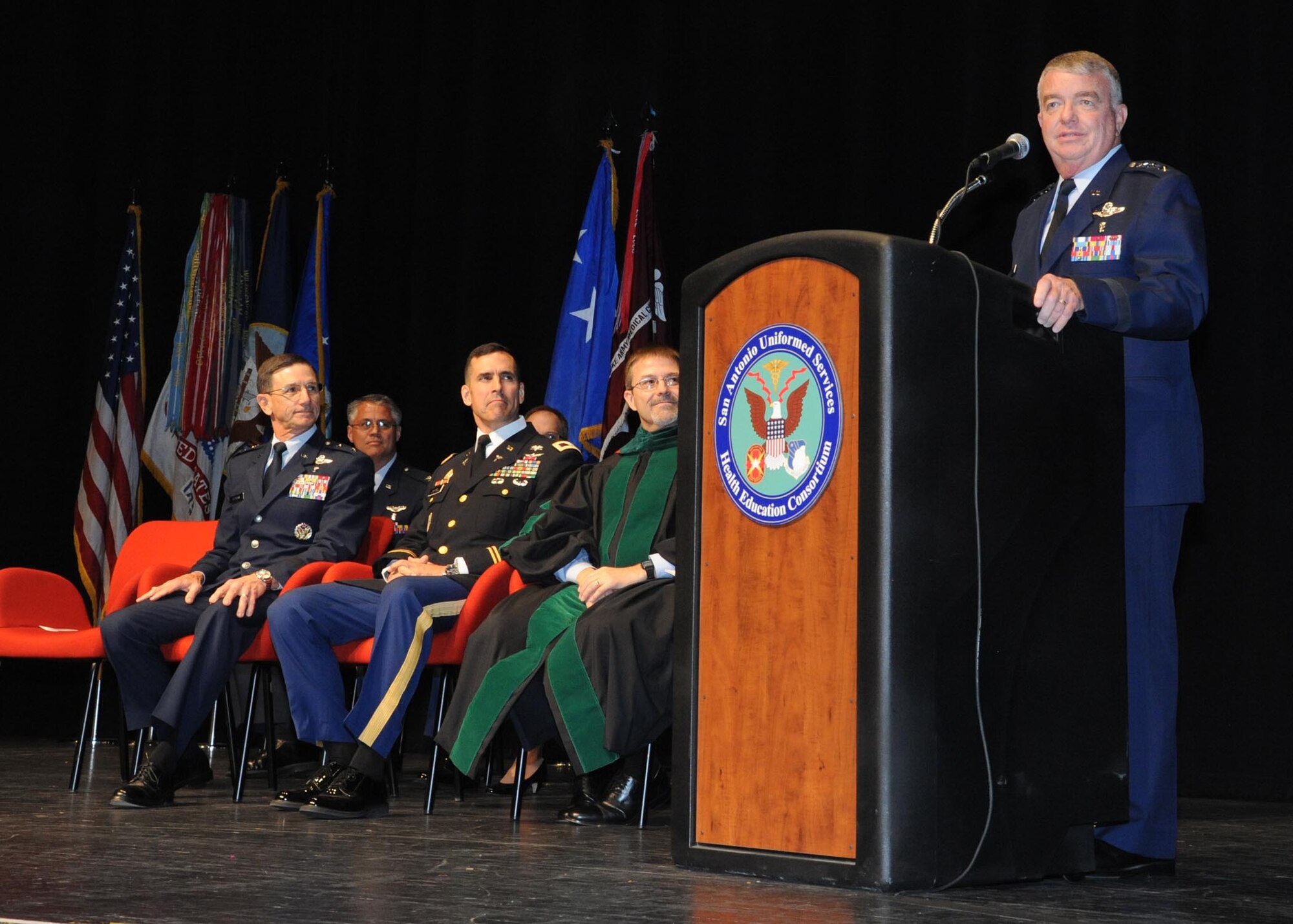 U.S. Air Force Lt. Gen. Thomas Travis delivers opening remarks during the San Antonio Uniformed Services Health Education Consortium graduation ceremony June 7 at the Lila Cockrell Theatre in San Antonio. Seated, from left to right, are Air Force Maj. Gen. Byron Hepburn, commander of the 59th Medical Wing and director of the San Antonio Military Health System, Army Col. Kyle Campbell, Brooke Army Medical Center commander, and Woodson Scott Jones, Dean of SAUSHEC. SAUSHEC is one of the largest graduate medical education programs in the nation with more than 35 programs and 600 residents in training. (U.S. Air Force photo/Richard McFadden)