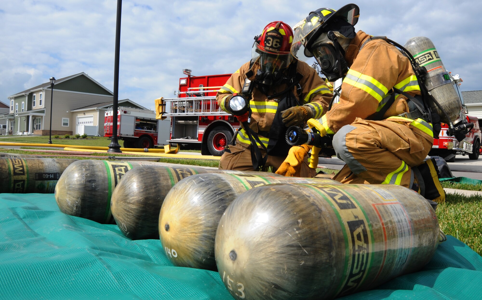 Firefighters from the 509th Civil Engineer Squadron set up oxygen tanks during a mock fire in base housing at Whiteman Air Force Base, Mo., June 7, 2013. The oxygen tanks allow the firefighters to breathe clean air while in a smoke-filled house. (U.S. Air Force photo by Airman 1st Class Bryan Crane/Released)