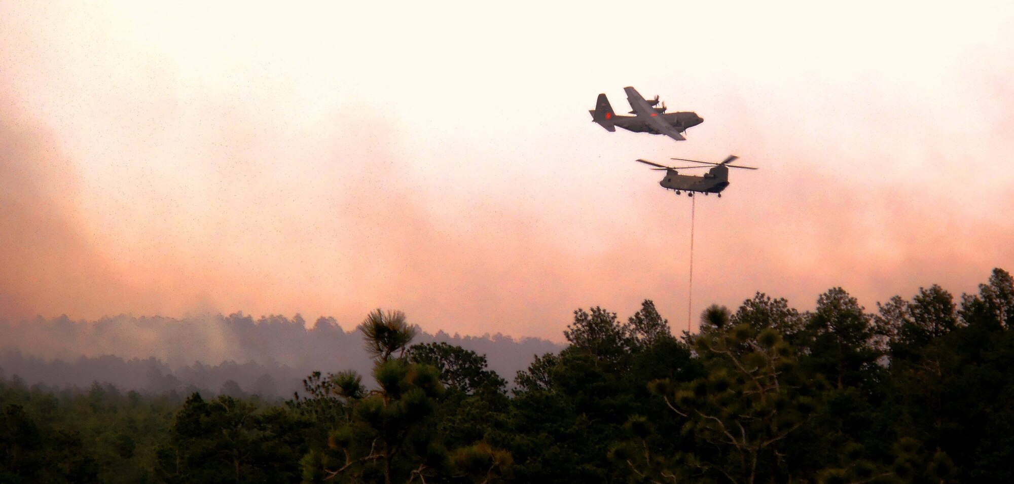 A Modular Airborne Fire Fighting System, or "MAFFS"-equipped C-130 departs the Black Forest fire June 12 after dropping a line of fire retardant in northern El Paso County, Colo. An Army CH-47 Chinook helicopter can be seen scooping up water in an effort to aide firefighting efforts. Manned by Airmen of the 302nd Airlift Wing, both the C-130 aircraft and members were activated to support wildland firefighting efforts through a request from the National Interagency Fire Center in Boise, Idaho. (Courtesy photo/Travis Leland)