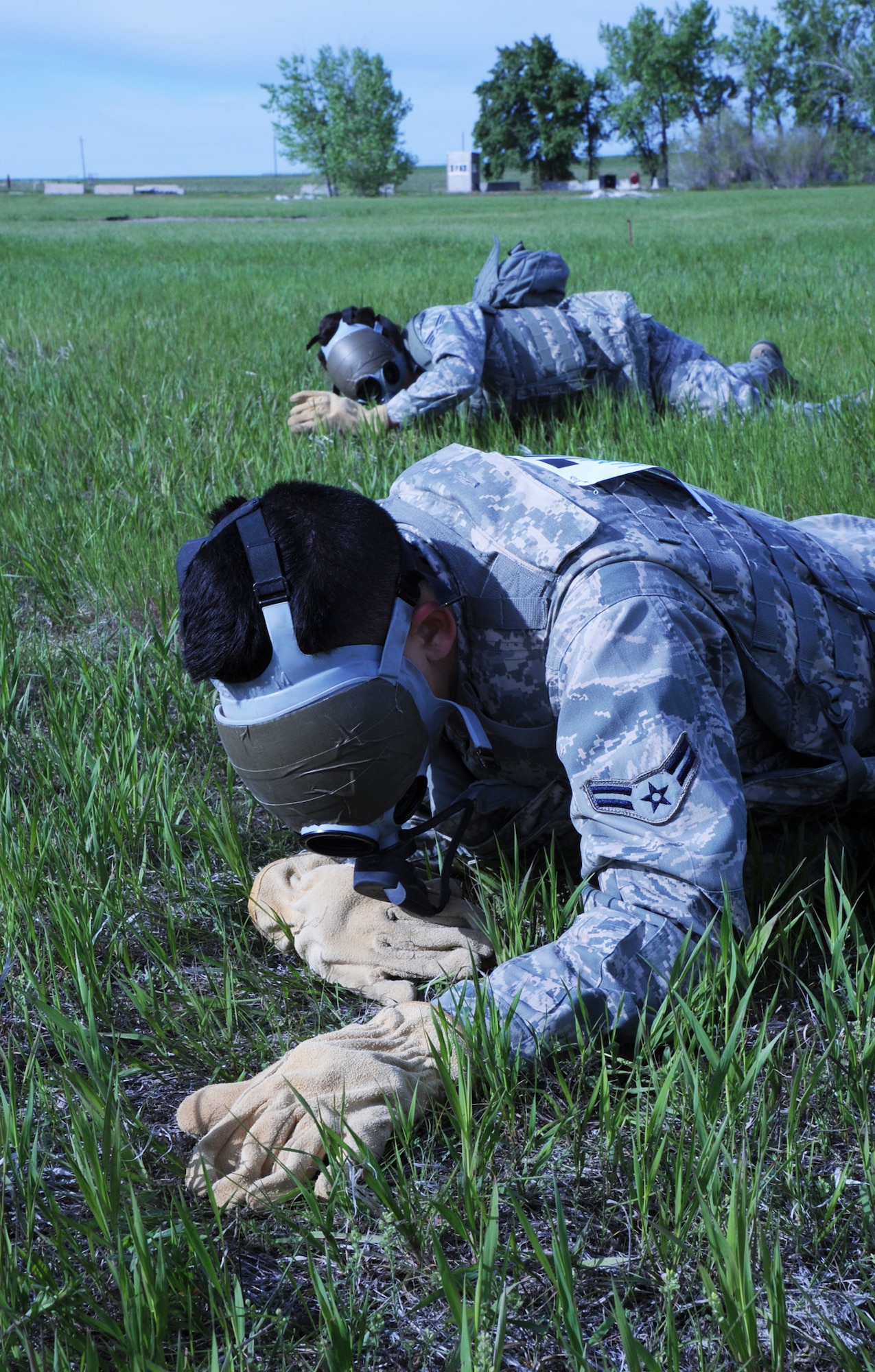 Airman 1st Class Darias Faaita, 741st Missile Security Forces Squadron member, and Senior Airman Mary Tarasiewicz, 741st MSFS member, (background) low-crawl through grass wearing blinded gas masks. Station 21 required competitors to work as a team, as communication was necessary in order to reach the target without any sight. (U.S. Air Force photo/Senior Airman Katrina Heikkinen)