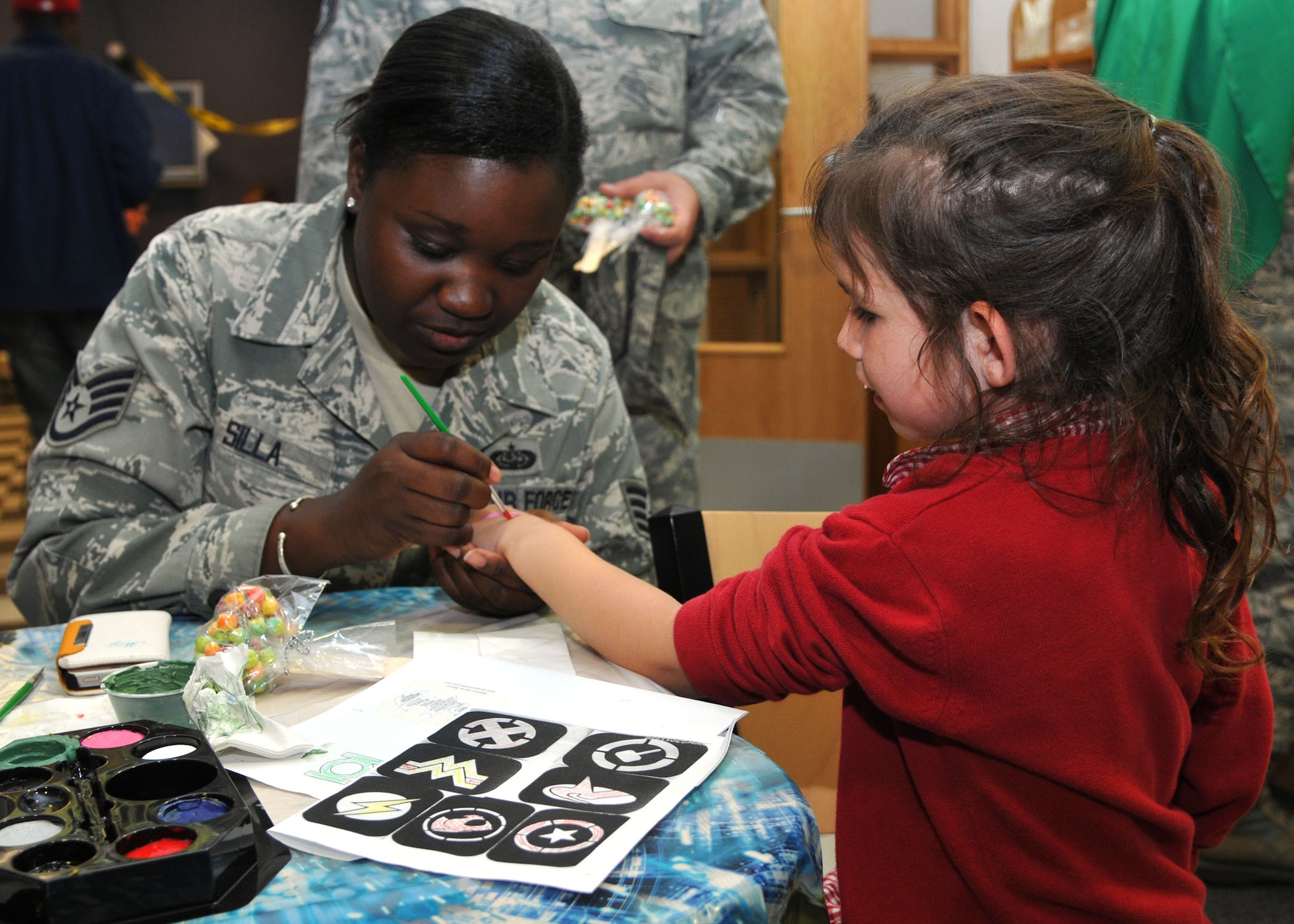 Elizabeth Bitson, 2, daughter of Master Sgt. Michael Bitson, 100th Communications Squadron Operations Flight assistant flight chief from Shelby, Mich., has her hand painted by Staff Sgt. Ndeye Silla, 100th CS NCO in charge of commanders support staff from Austin, Texas, during the Hearts Apart dinner June 12, 2013, at the bowling alley on RAF Mildenhall, England. The dinner had multiple activity stations including coloring, face painting and temporary tattoos. (U.S. Air Force photo by Airman 1st Class Kelsey Waters/Released)