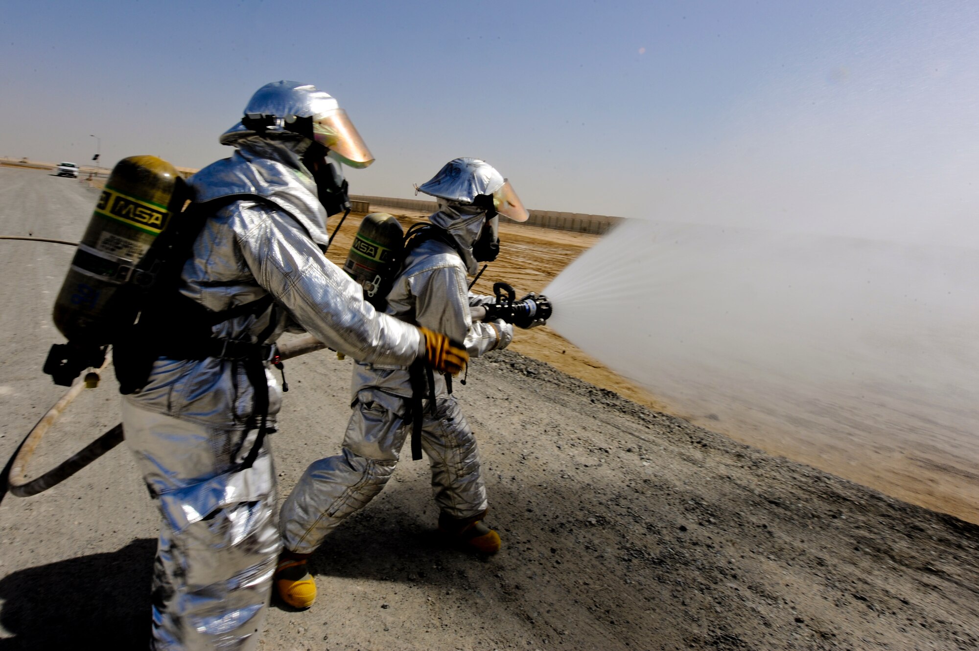 U.S. Air Force Airman 1st Class Chris Parker (on the nozzle) and U.S. Air Force Staff Sgt. Aaron Theriault, both 380th Expeditionary Civil Engineer Squadron firefighters, spray a simulated fire during a training exercise at an undisclosed location in Southwest Asia June 10, 2013. The exercise tested the team’s response time and capability to perform under possible real world situations.  Parker is a native of Wilson, N.C., and is deployed from Seymour Johnson Air Force Base, N.C.  Theriault hails from Fargo, N.D., and is deployed from Yokota Air Base, Japan. (U.S. Air Force photo by Staff Sgt. Joshua J. Garcia)