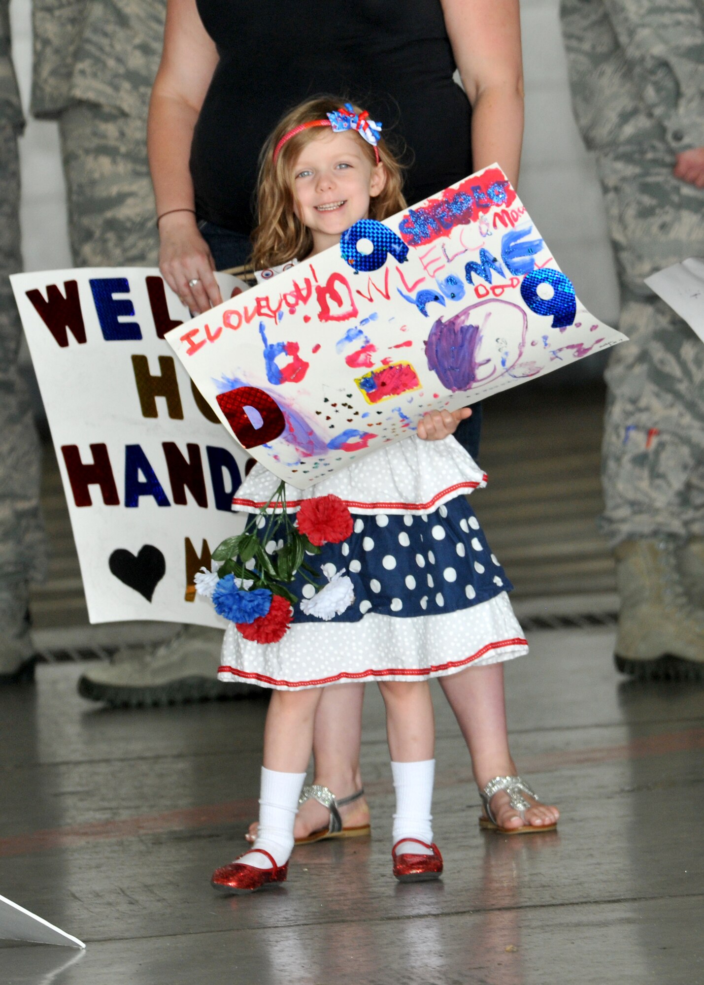 Abby, daughter of a U.S. Air Force staff sergeant assigned to the 97th Intelligence Squadron, holds up a welcome back sign for her dad in the Bennie Davis Maintenance Facility at Offutt Air Force Base, Neb., June 14,. Team Offutt family members, friends and coworkers welcomed nearly 200 Airmen upon their return from a deployment to Southwest Asia. (U.S. Air Force photo by Tech. Sgt. Markus M. Maier/Released)