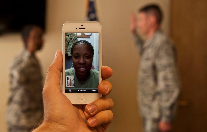 U.S. Air Force Staff Sgt. Ashley Charles, 451st Air Expeditionary Wing services specialist, Kandahar Airfield, Afghanistan, watches via live video stream as her husband, Staff Sgt. Michael Charles, 99th Air Base Wing Public Affairs photojournalist, re-enlists with Lt. Col. Jonathan Jehn, 99th Comptroller Squadron commander, June 14, 2013, at Nellis Air Force Base, Nev. This is Charles’ first re-enlistment. Deployed military members increasingly rely on such technology to witness loved ones’ significant life events. (U.S. Air Force photo by Senior Airman Daniel Hughes)