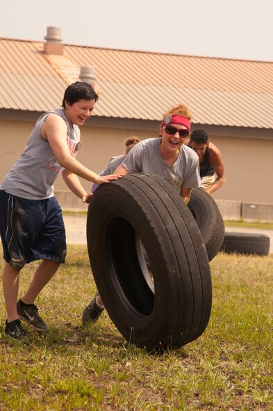 Airman 1st Class’ Victoria Rosenbaum and Rachelle Zallar, 8th Communication Squadron members, laugh their way through the fourth obstacle of the Wolf Pack Warrior Mud Run at Kunsan Air Base, Republic of Korea, June 8, 2013. This particular team rolled their tire to the other side of the yard, with the other half of their team close behind. (U.S. Air Force photo by Senior Airman Jessica Haas/ Released)